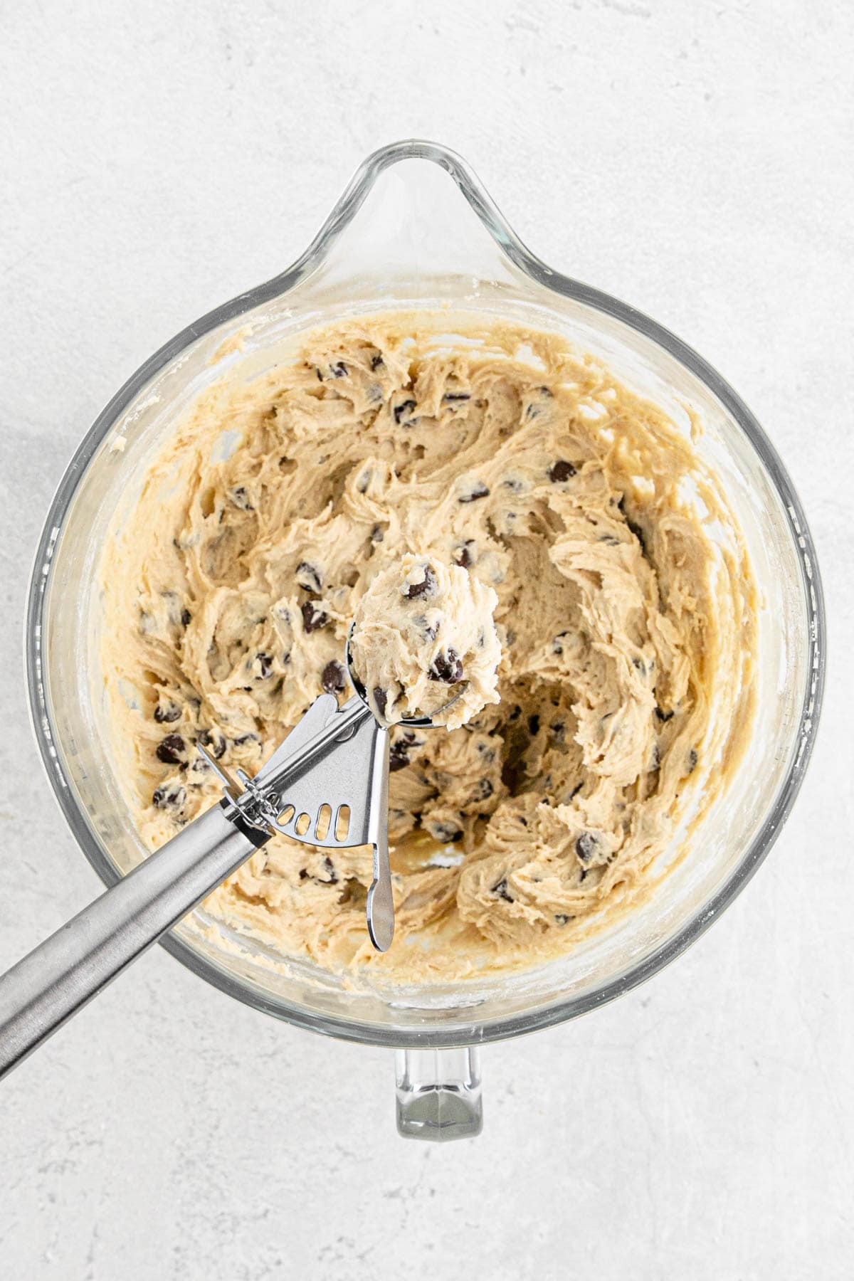 Cookie scoop resting on a bowl of finished chocolate chip cookie dough