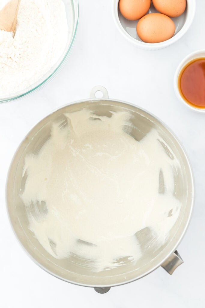 Beaten butter and sugar and oil in a mixing bowl on white countertop with eggs in a bowl