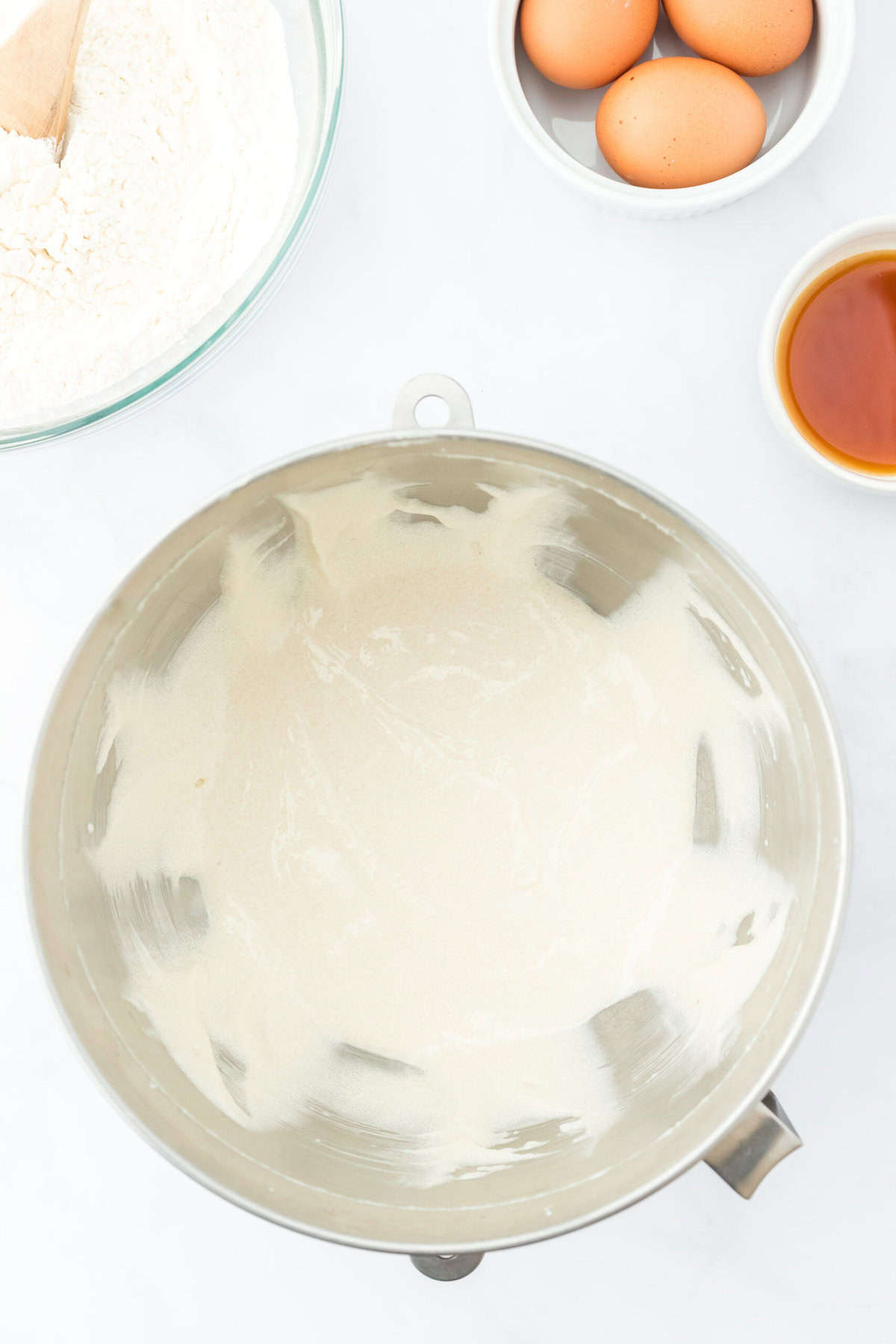 Beaten butter and sugar and oil in a mixing bowl on white countertop with eggs in a bowl