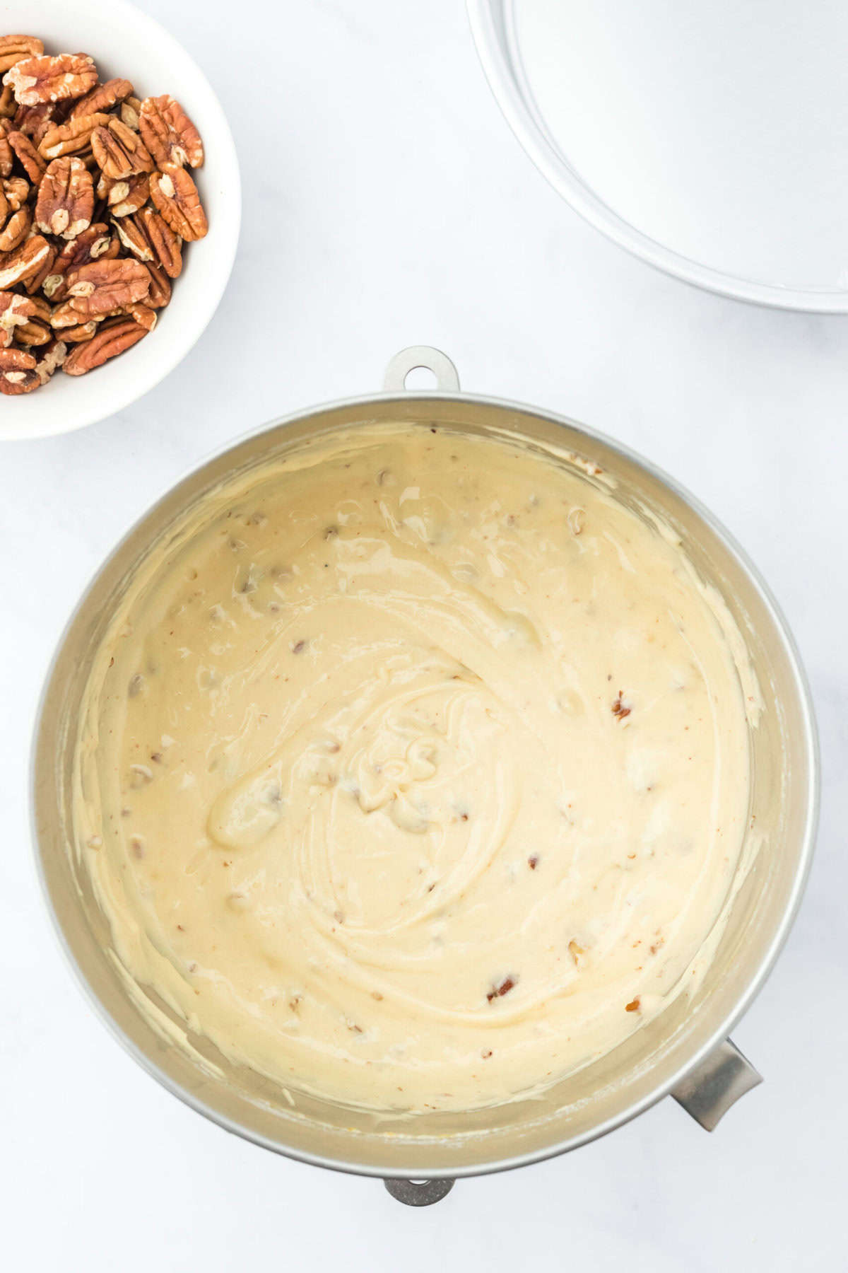 Butter pecan cake batter mixed together until smooth on white countertop with pecans in a white bowl nearby