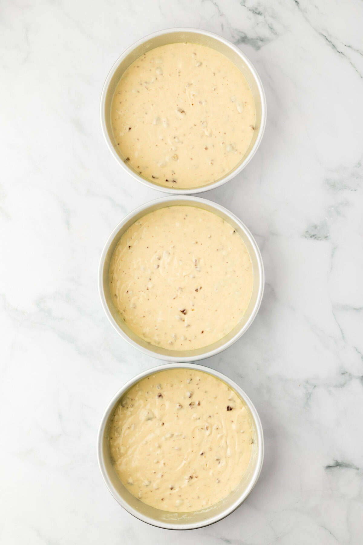 Pecan cake batter added to three round pans on white countertop