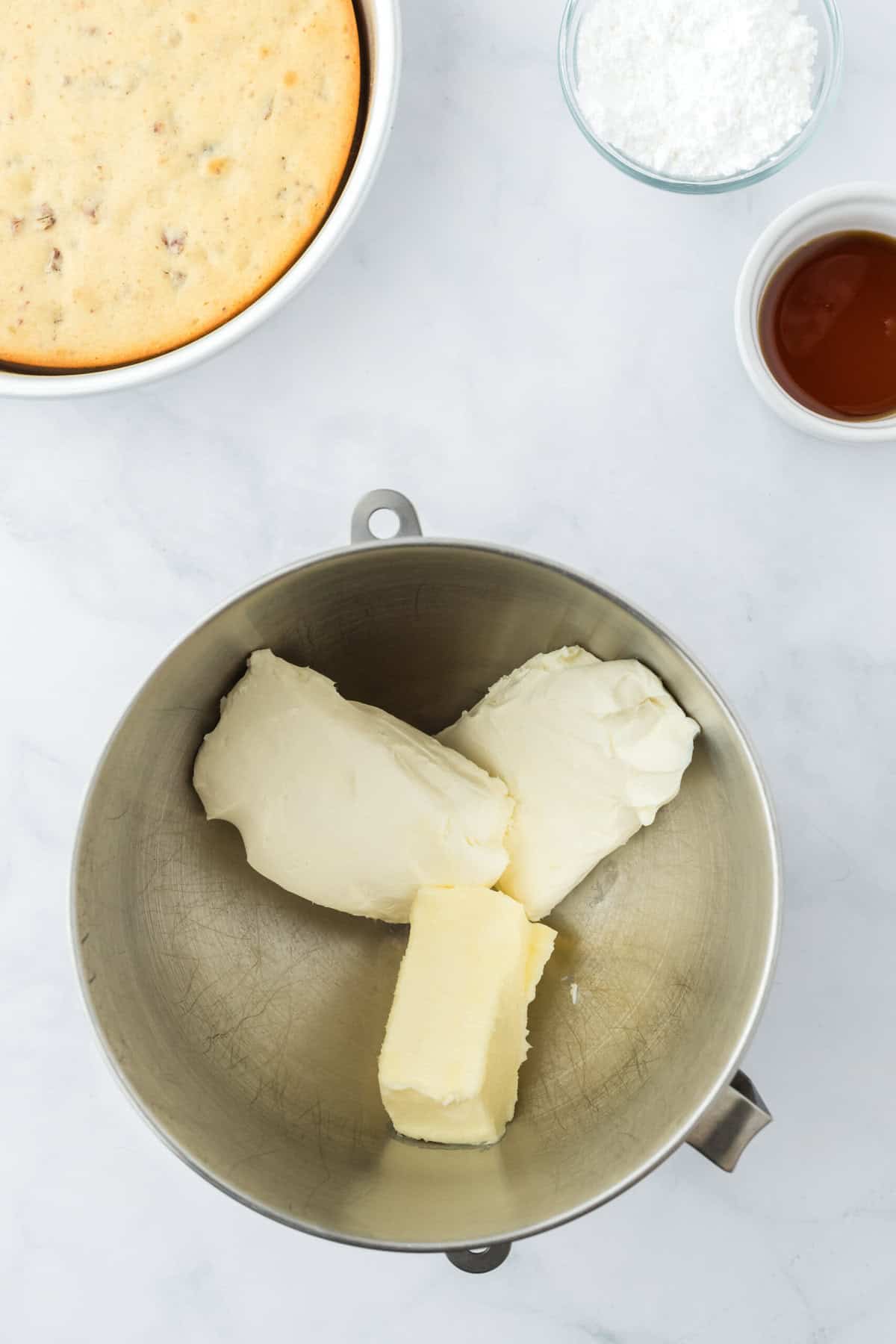 Butter and cream cheese added to a stand mixer bowl on white countertop