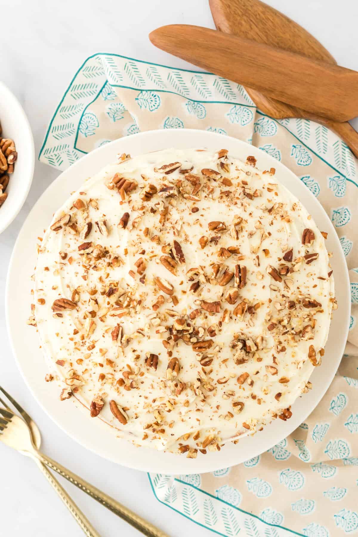 Frosted butter pecan layer cake with patterned napkin underneath on white background