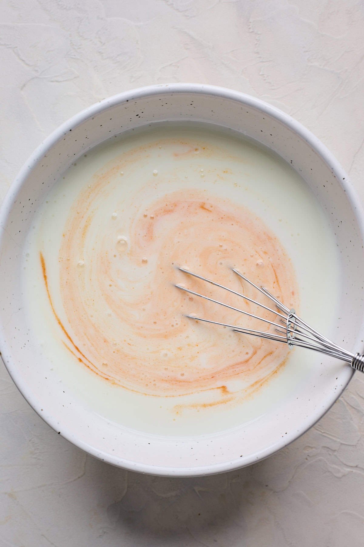 Hot sauce whisking into buttermilk in a white bowl