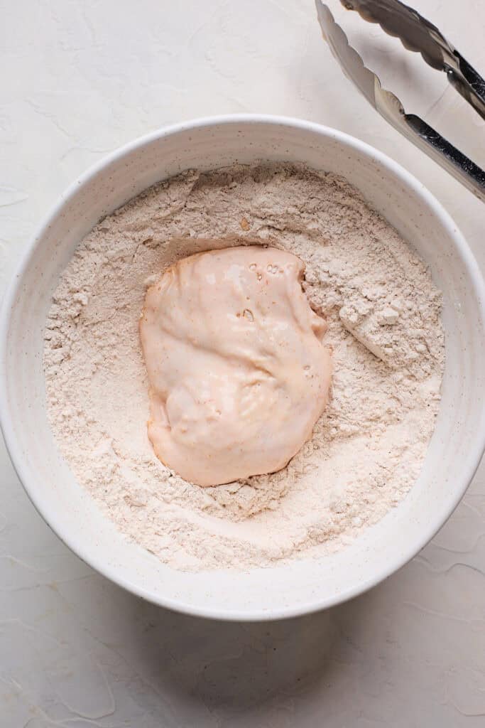 Battered chicken piece in seasoned flour bowl