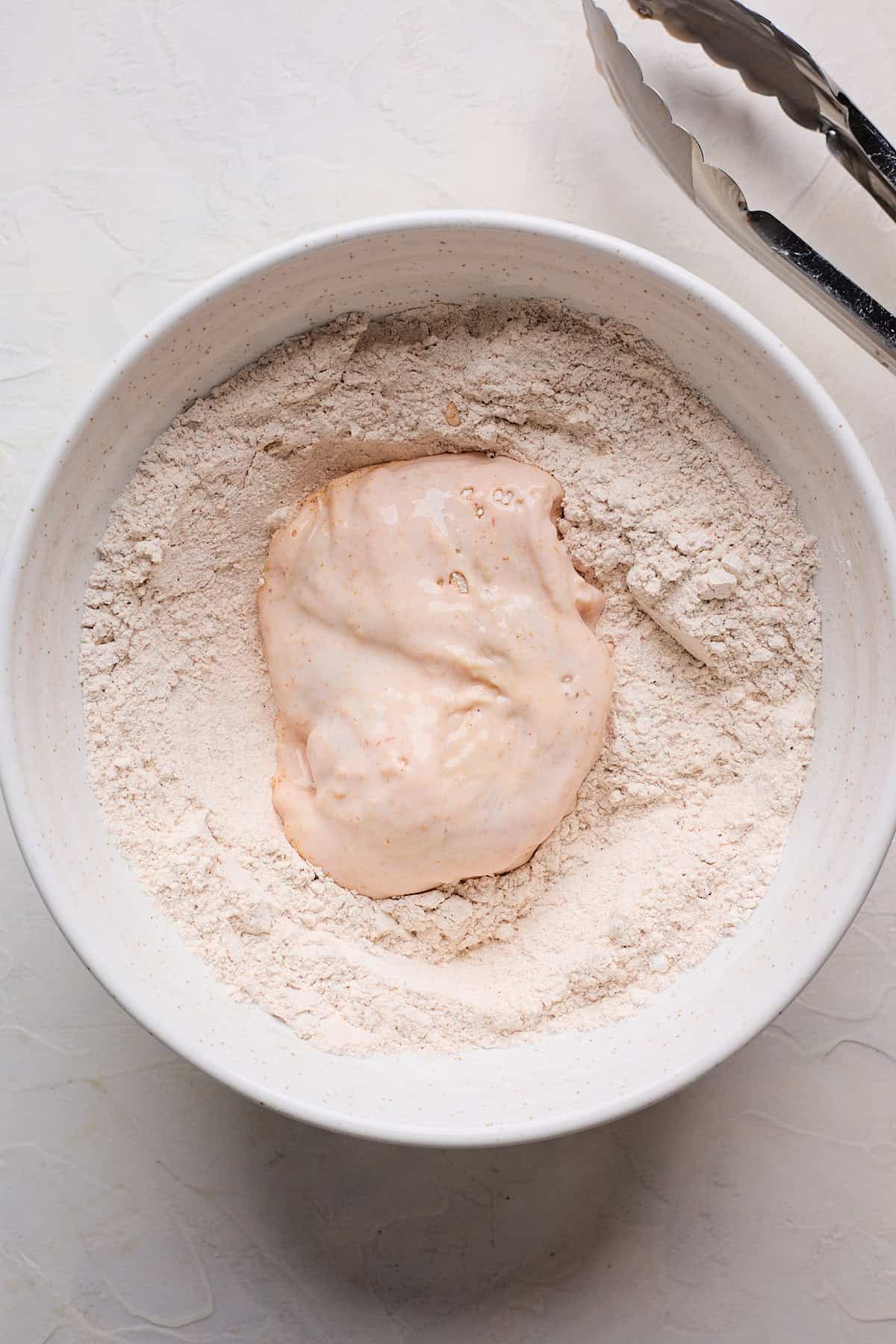 Battered chicken piece in seasoned flour bowl