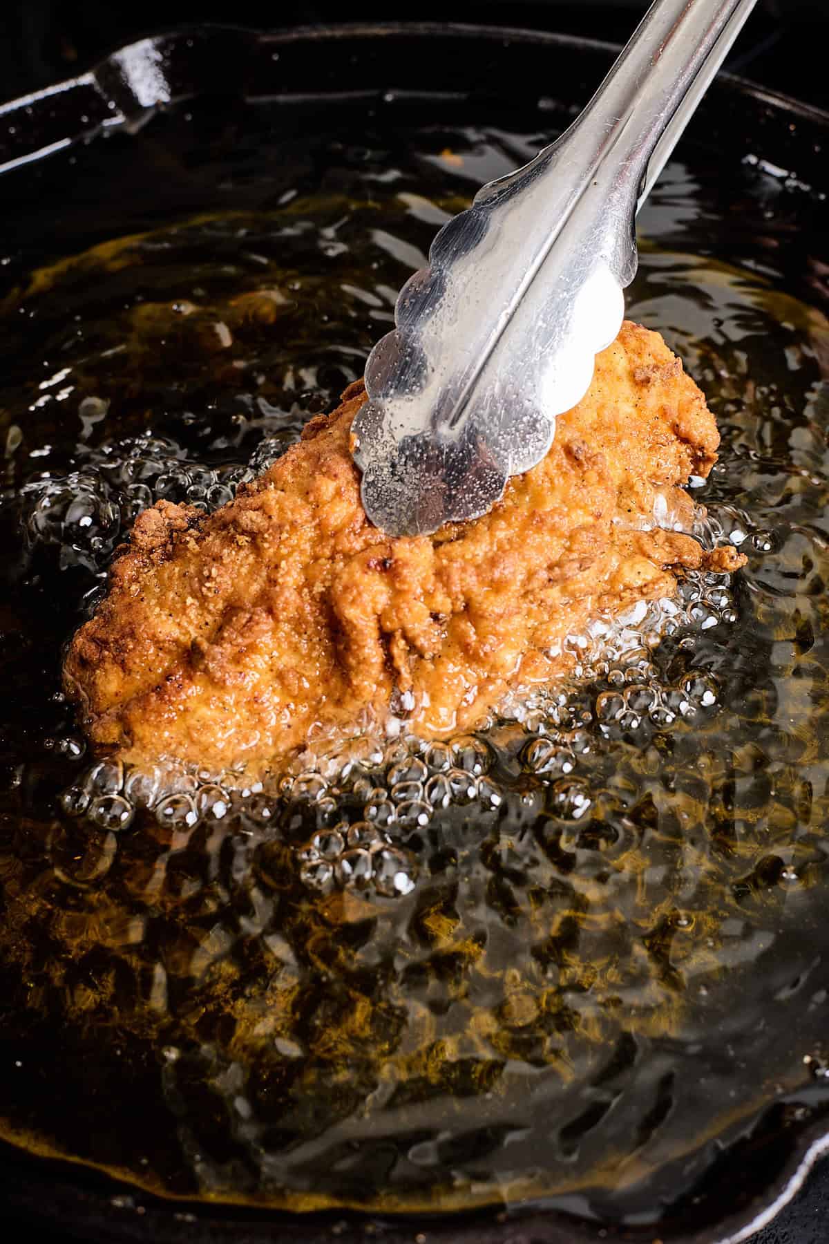 Chicken frying in hot oil with tongs being lifted