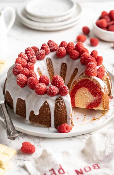 White chocolate raspberry bundt cake with slice missing on a white plate