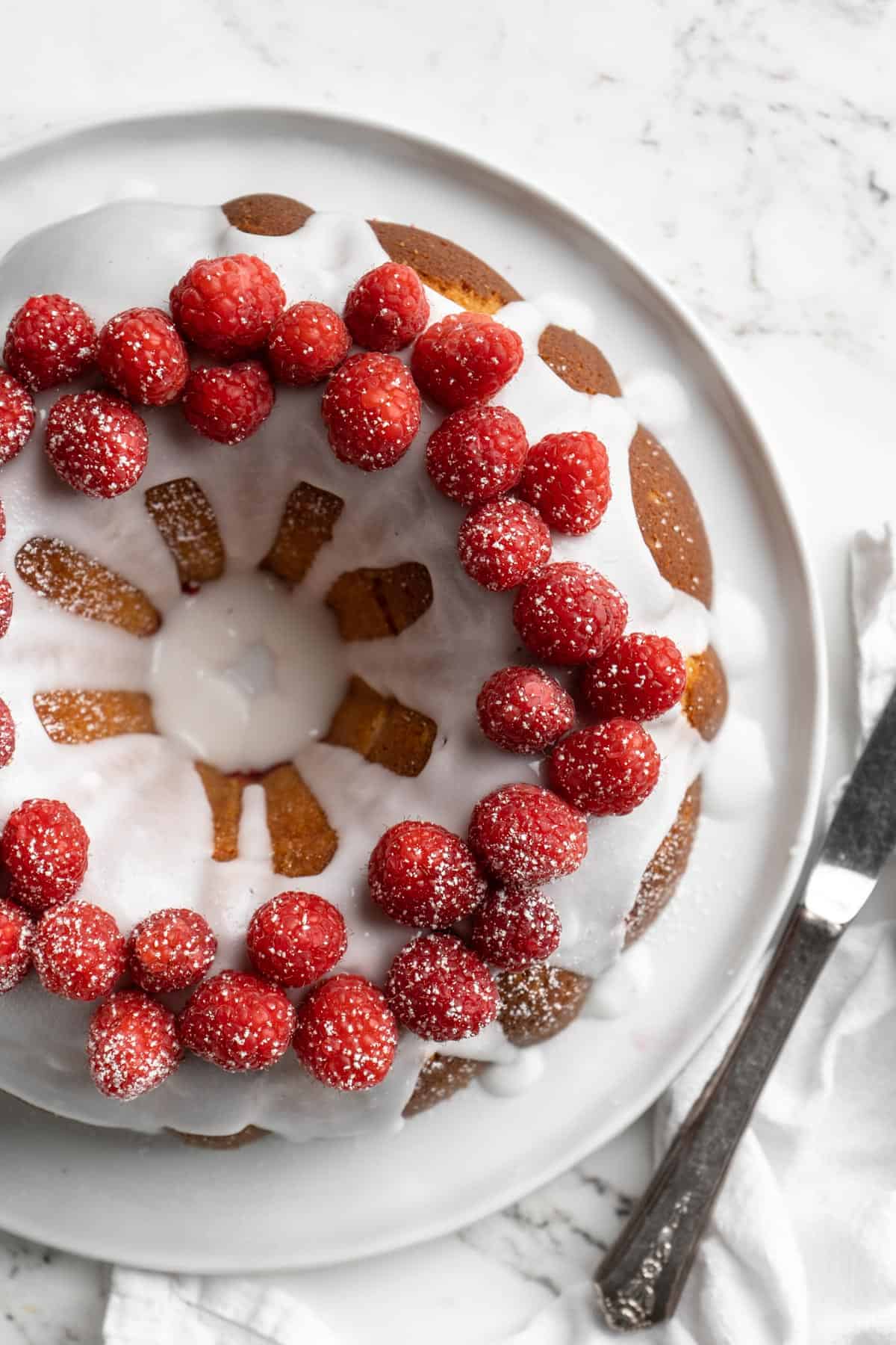 Overhead shot of the white chocolate raspberry bundt cake on a white plate with a knife next to it