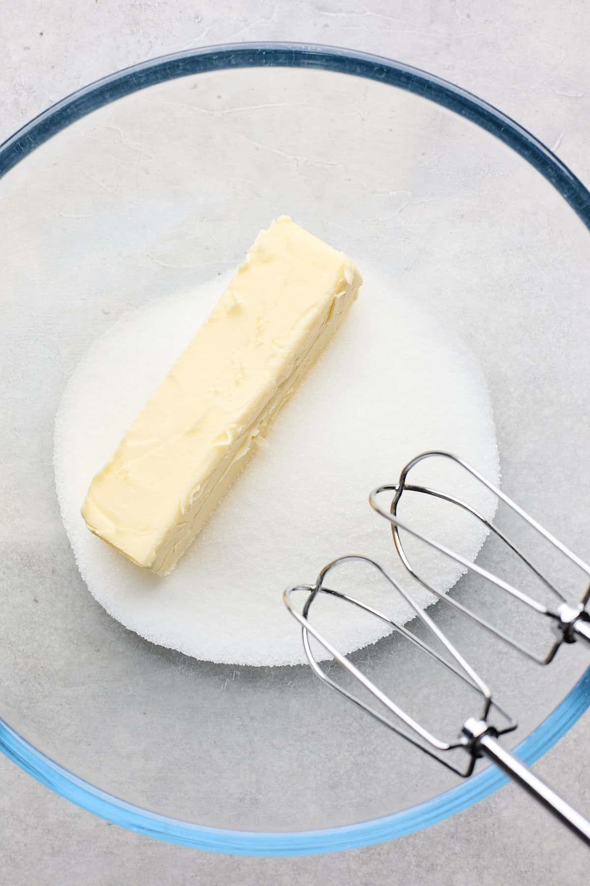 Butter and granulated sugar in a glass bowl with a hand mixer about to mix it