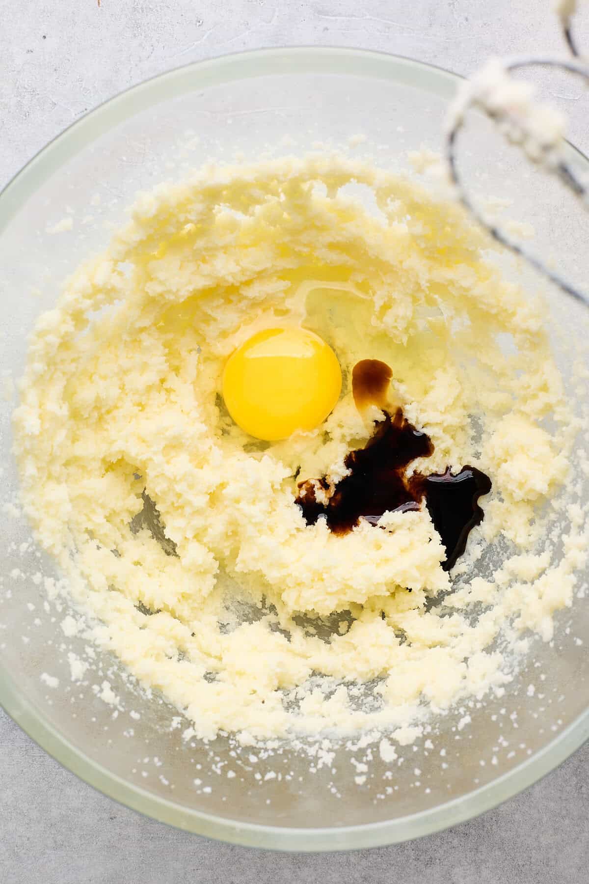 Egg in a glass bowl with vanilla extract and creamed butter and sugar being mixed