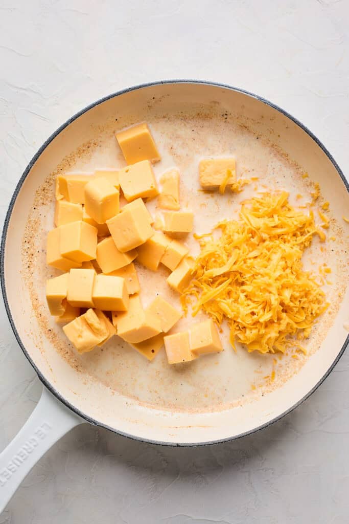 Velveeta and shredded cheddar cheese added to milk and spices in a large skillet