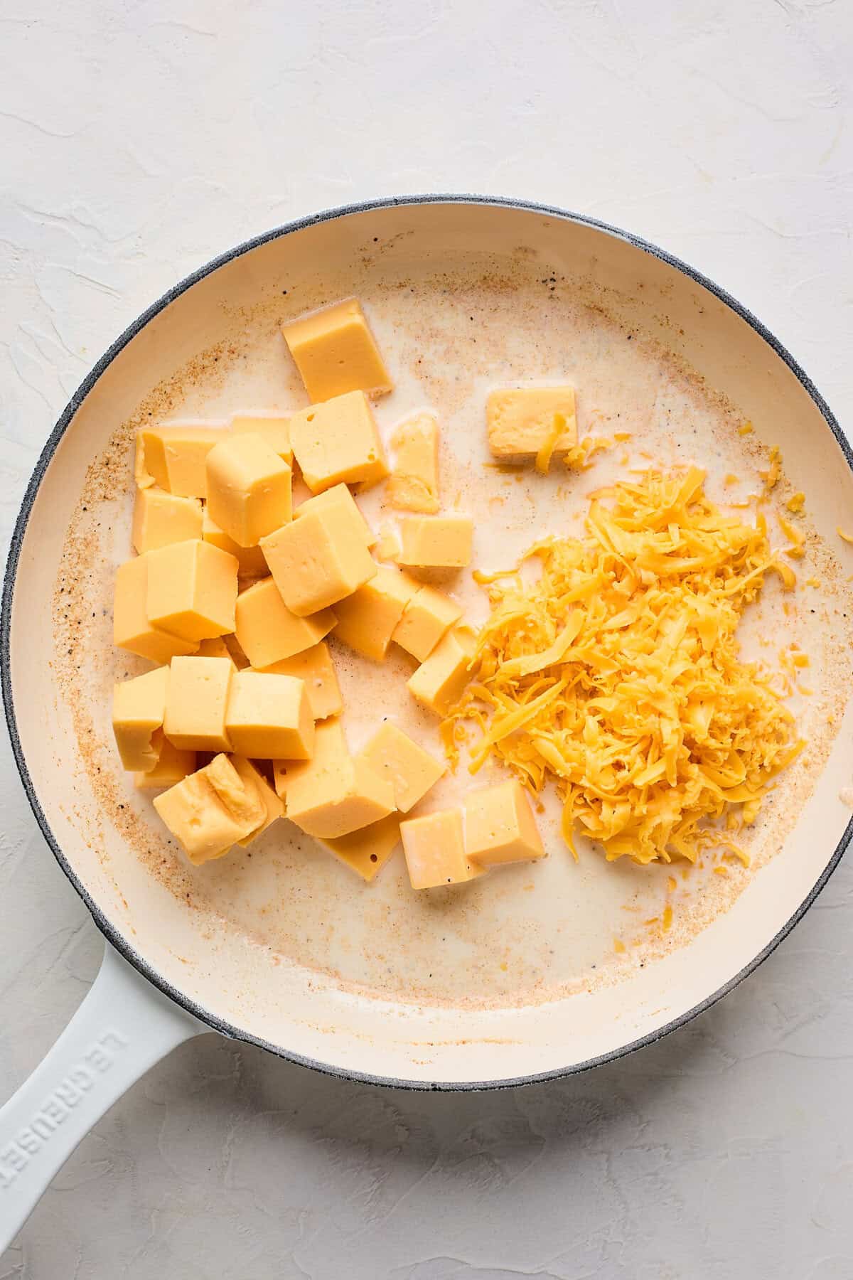 Velveeta and shredded cheddar cheese added to milk and spices in a large skillet