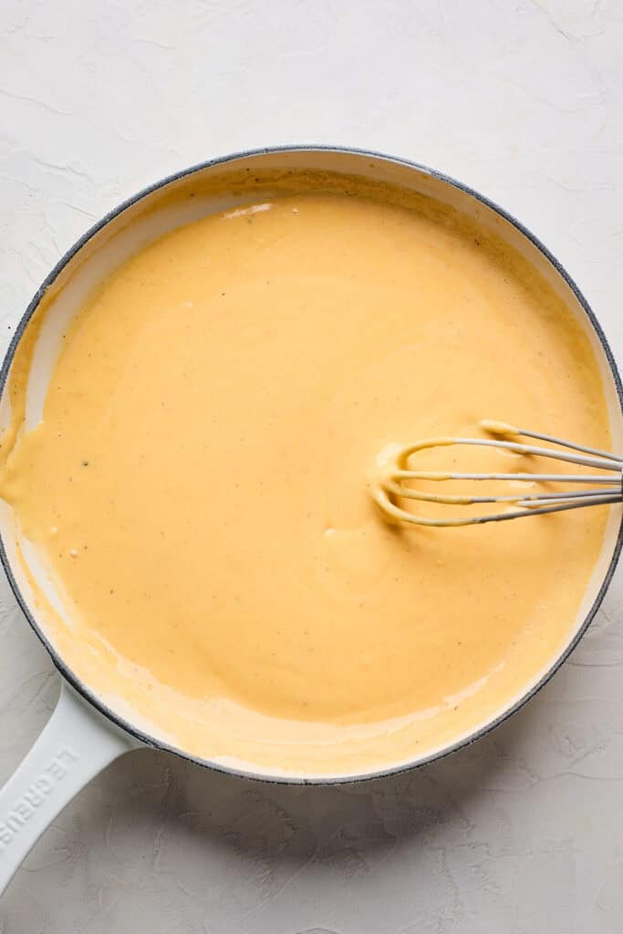 Smooth cheese sauce with a whisk in a skillet