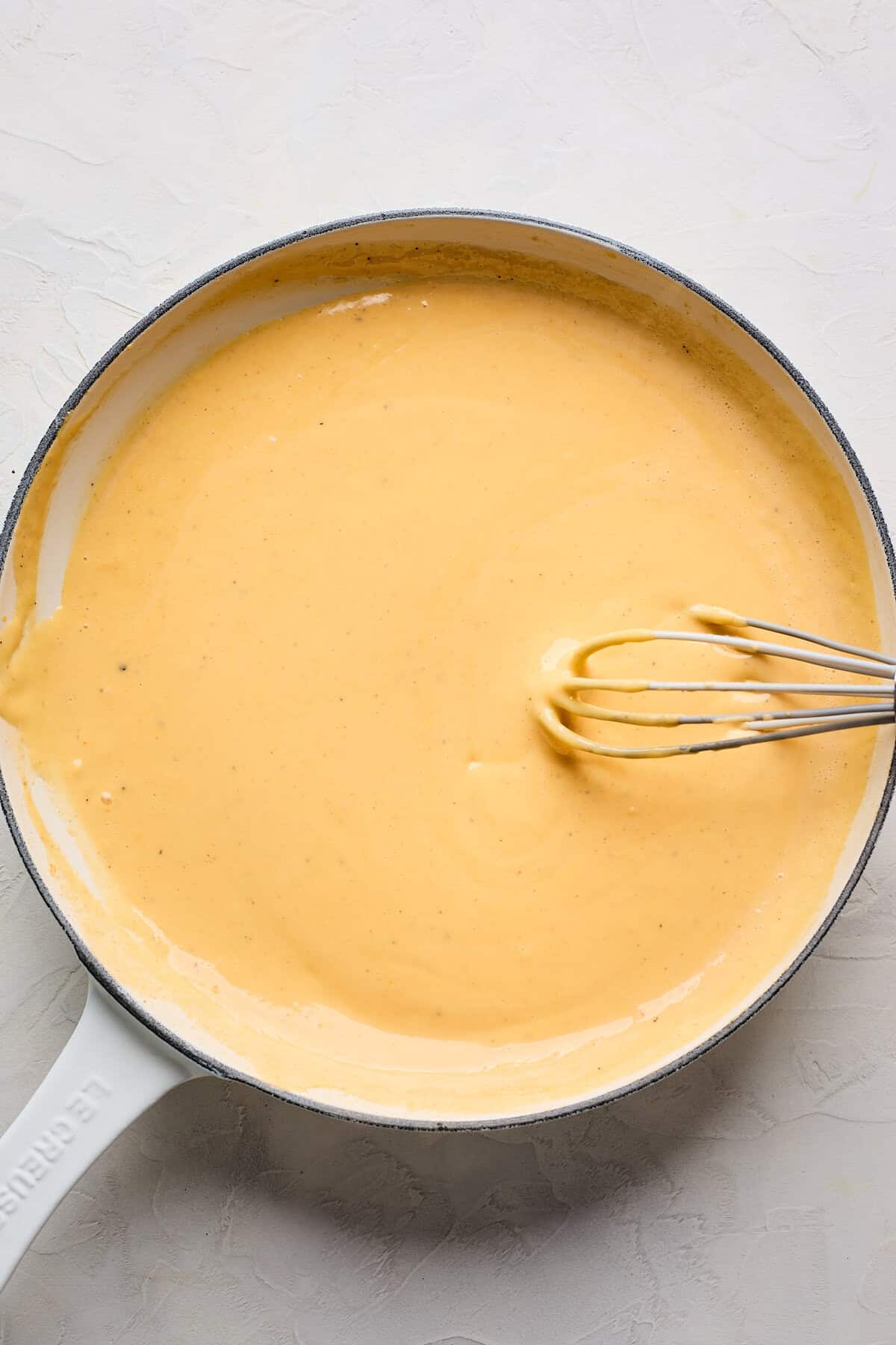 Smooth cheese sauce with a whisk in a skillet