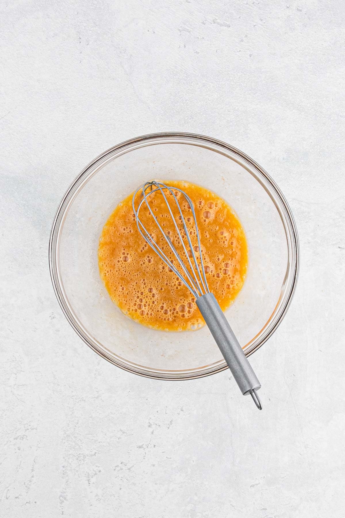 A metal whisk resting in a bowl of fully mixed eggs and seasoning