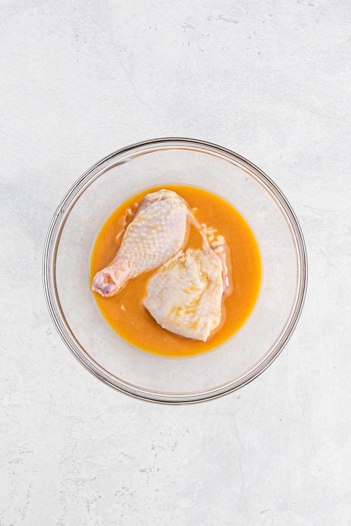 Chicken pieces soaking in an egg marinade in a glass bowl