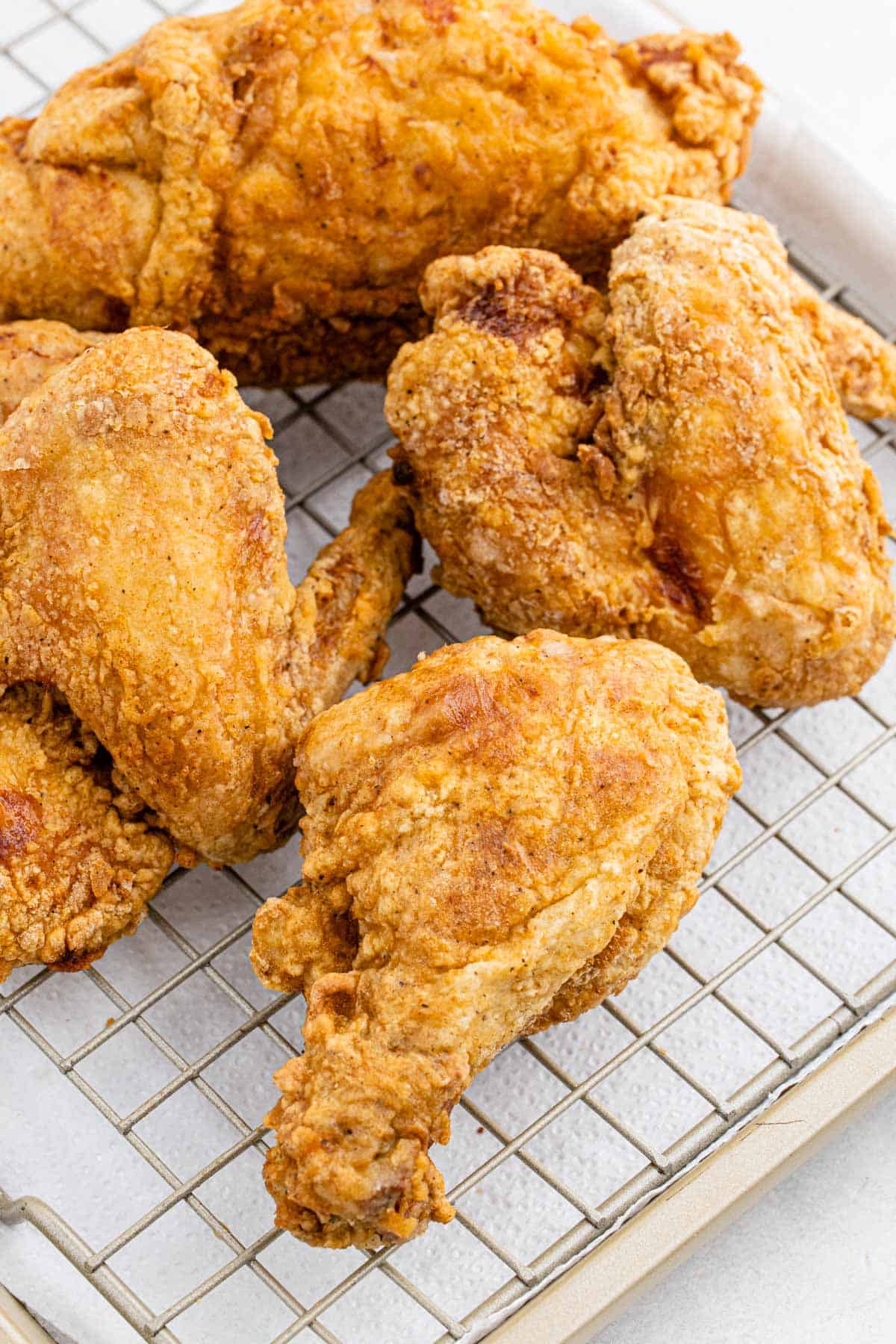 Crispy, golden brown fried chicken cooling on a wire rack over a baking sheet