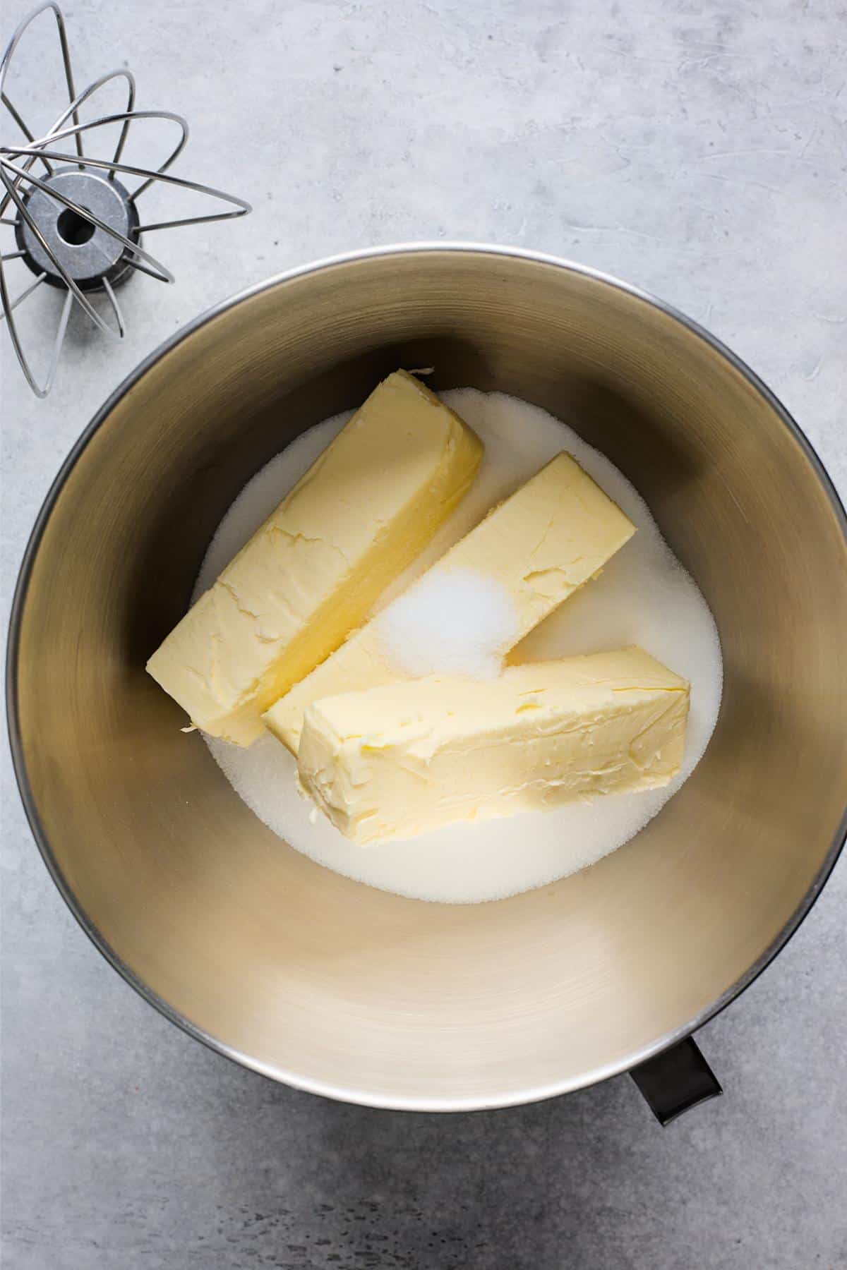 Butter sticks and sugar in a metal mixing bowl, ready to be creamed together