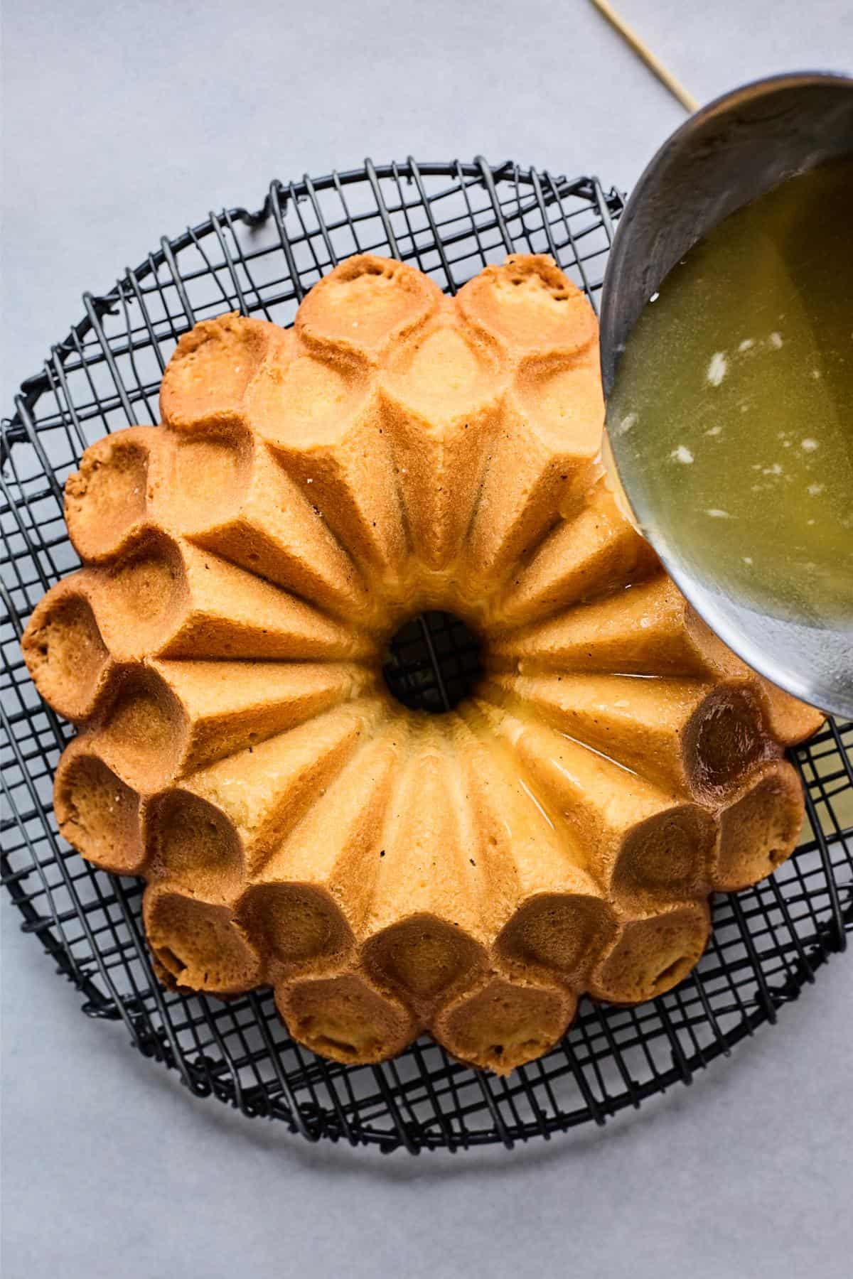 Glaze being poured over the bundt cake on a wire rack, dripping along the sides