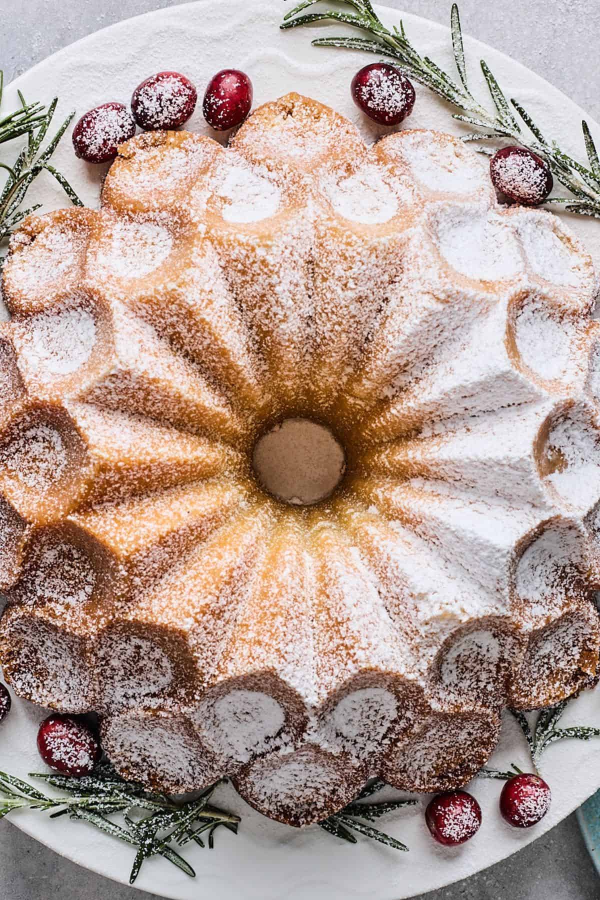 Finished eggnog cake, dusted with powdered sugar and garnished with fresh cranberries and rosemary sprigs