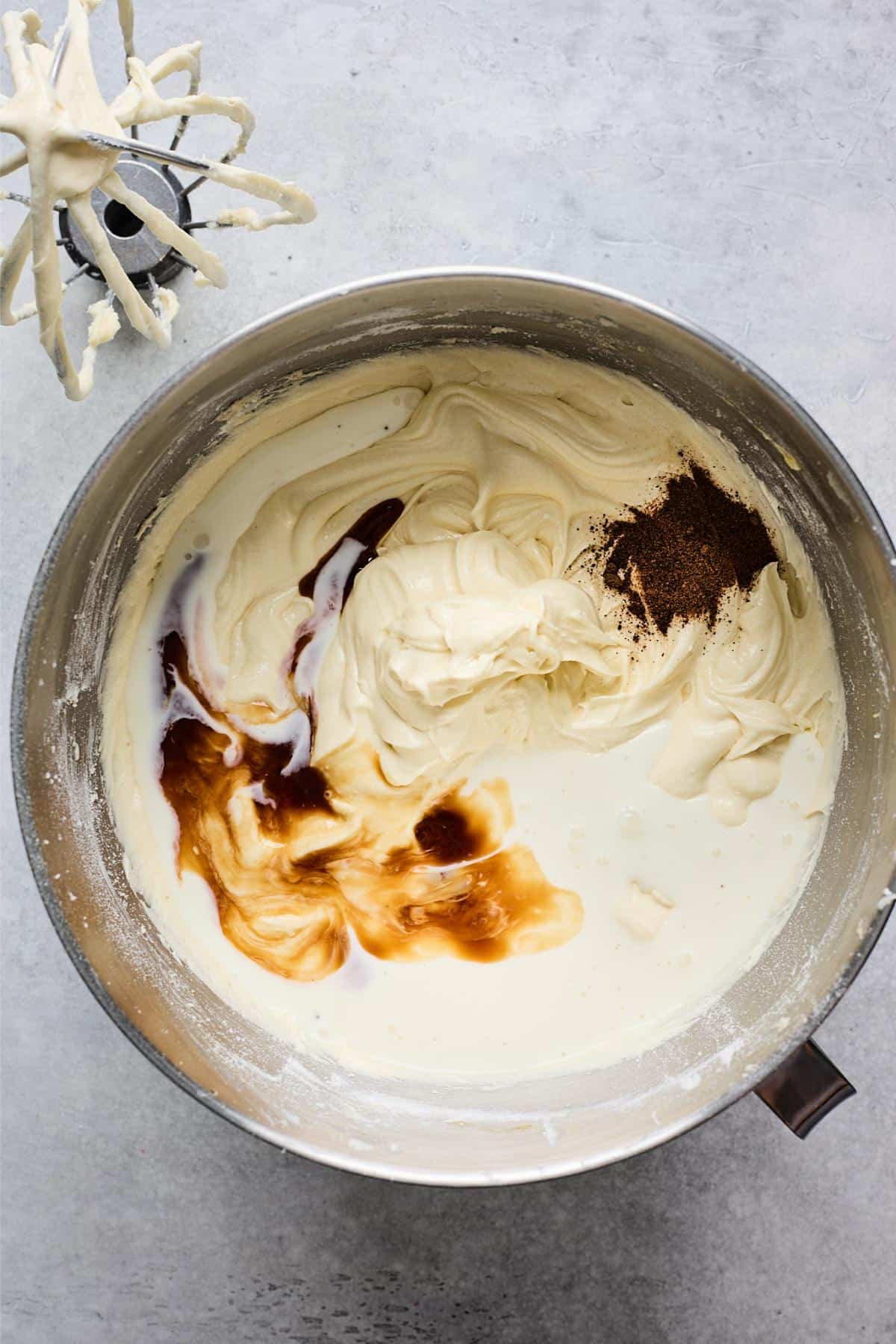 Smooth batter with added liquid ingredients and spices, showing swirls of vanilla and nutmeg in a mixing bowl