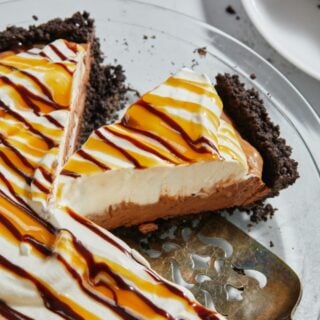 A slice of chocolate mousse pie drizzled with caramel and chocolate sauce being lifted off the pie, showing the creamy texture and the crumbly chocolate crust