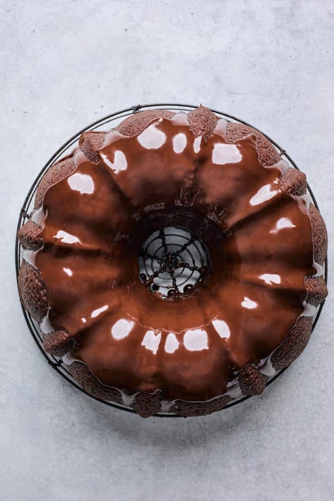 A Bundt cake covered in a shiny chocolate ganache glaze, resting on a cooling rack