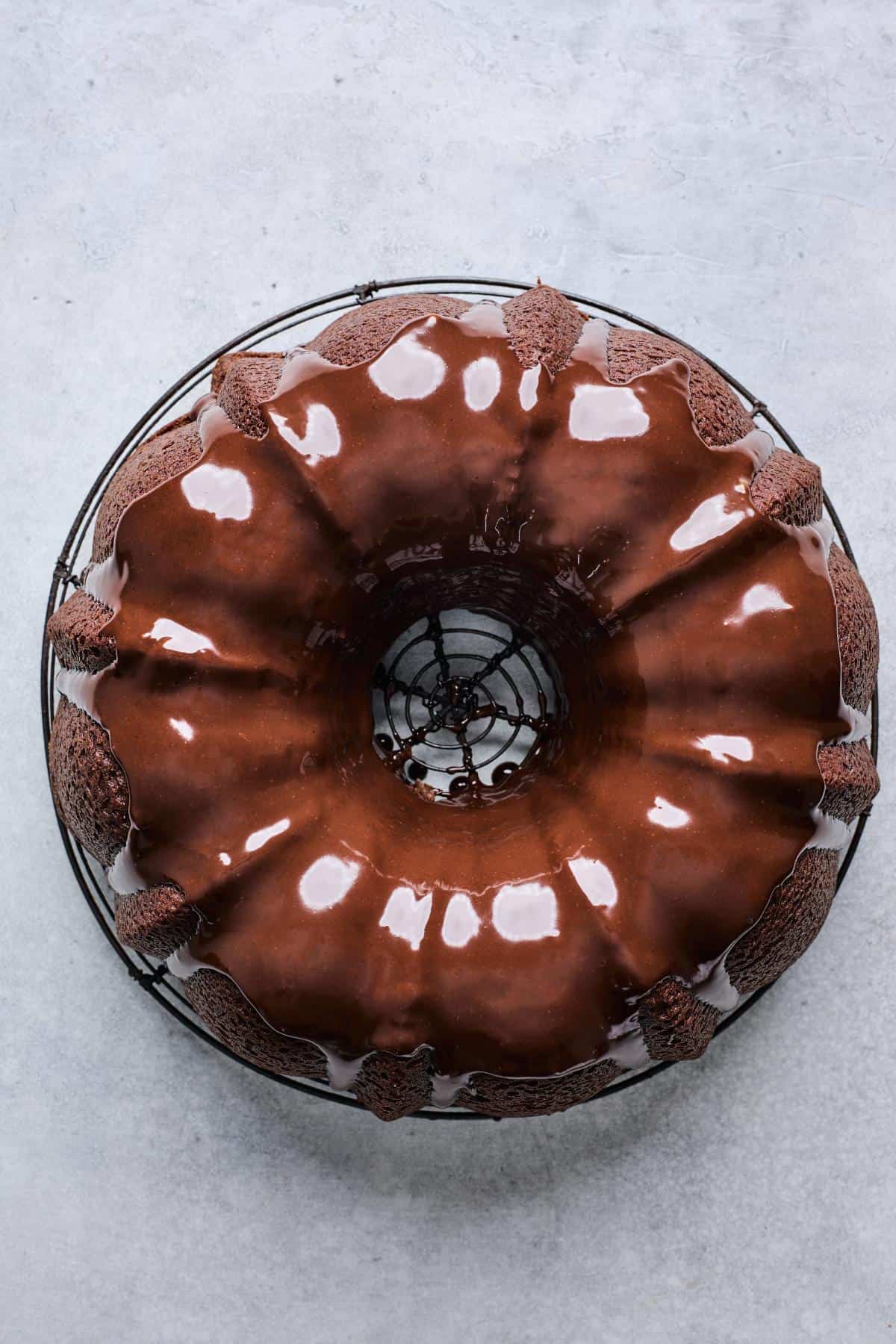 A Bundt cake covered in a shiny chocolate ganache glaze, resting on a cooling rack