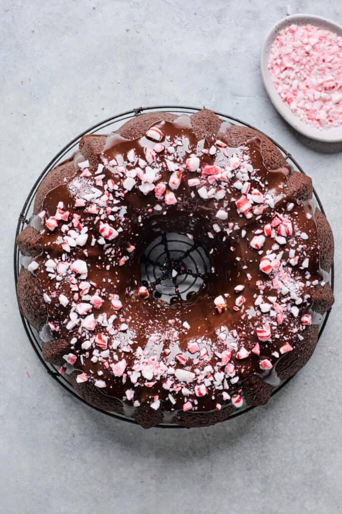 Chocolate peppermint cake with chocolate ganache glaze, topped with crushed peppermint candy, on a cooling rack