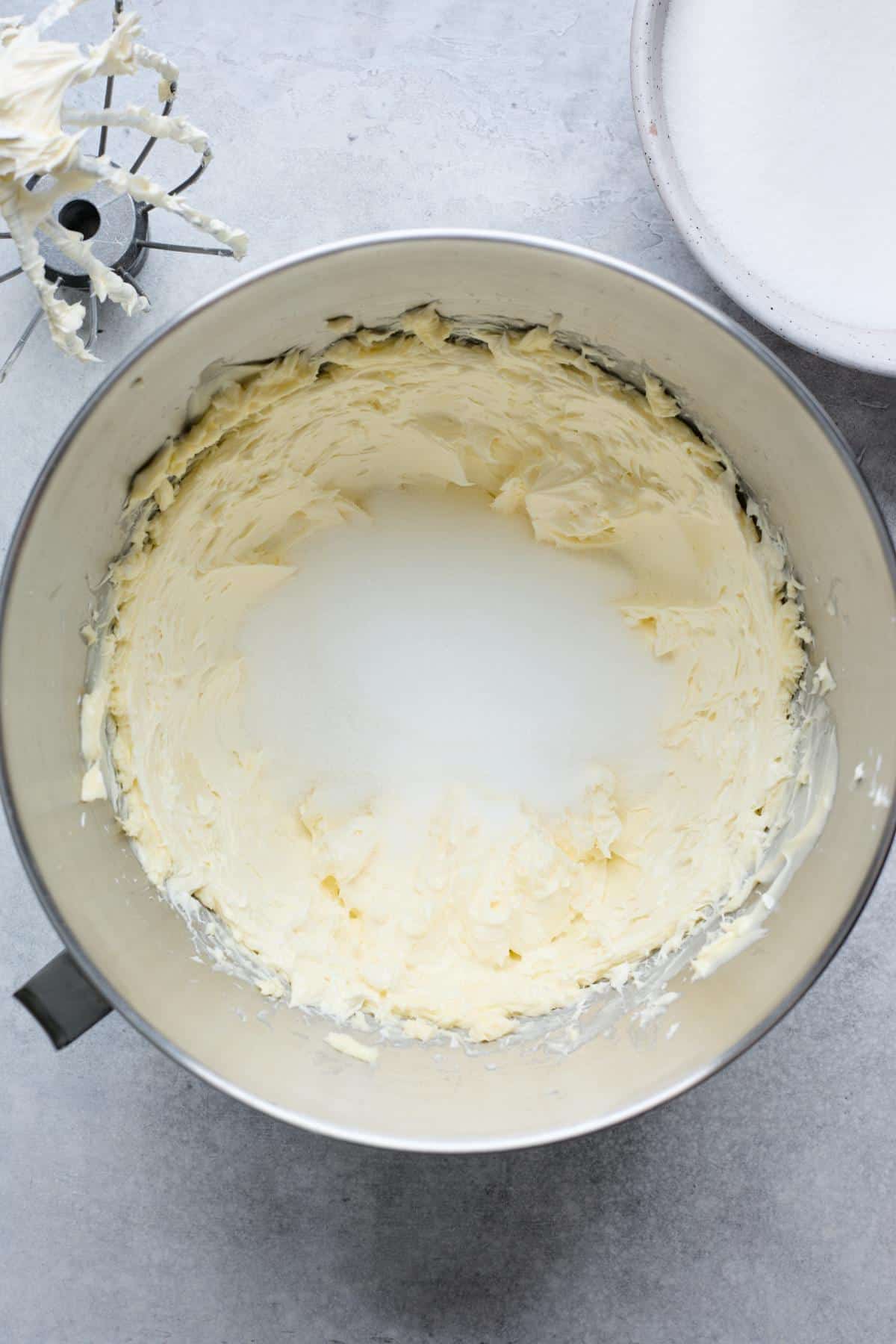 Creamed butter in a mixing bowl, with sugar poured in the center, ready for mixing