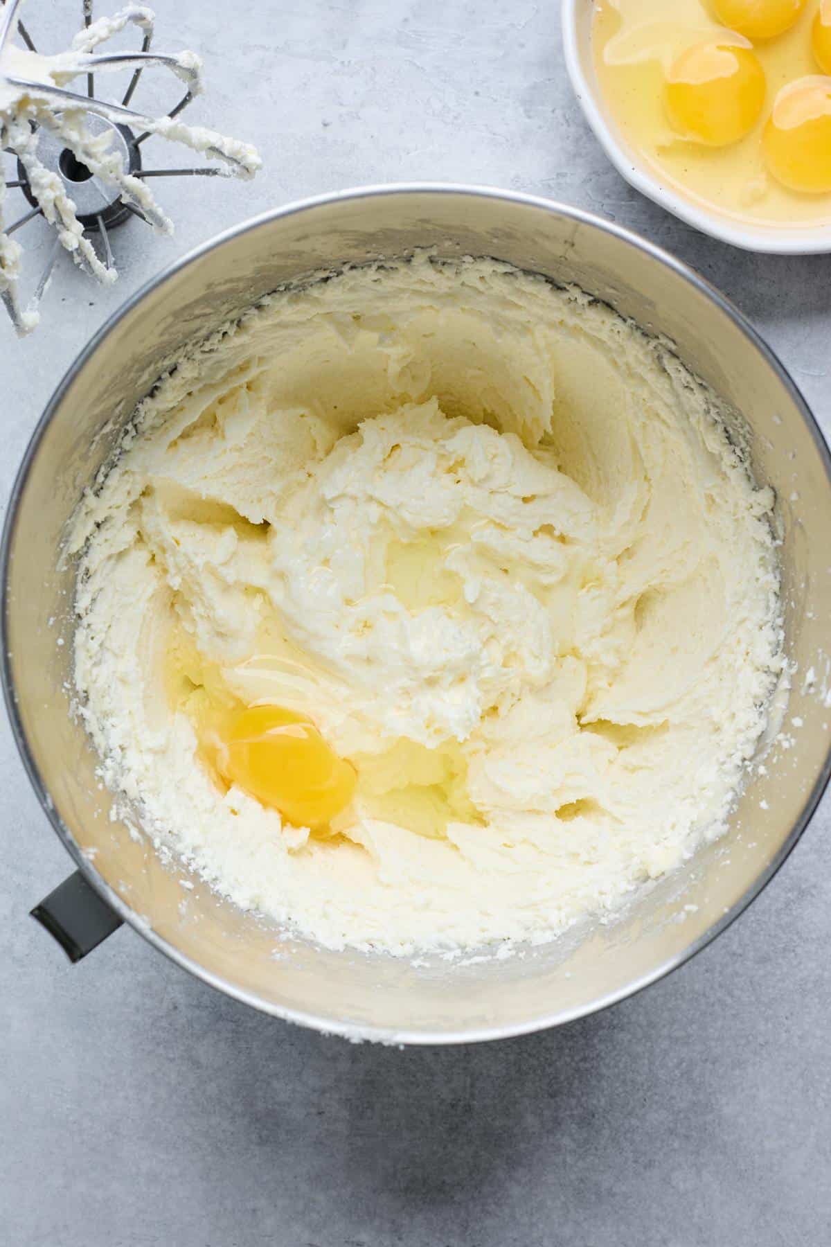 Creamed butter and sugar mixture with an egg cracked into the center, surrounded by additional eggs in a bowl