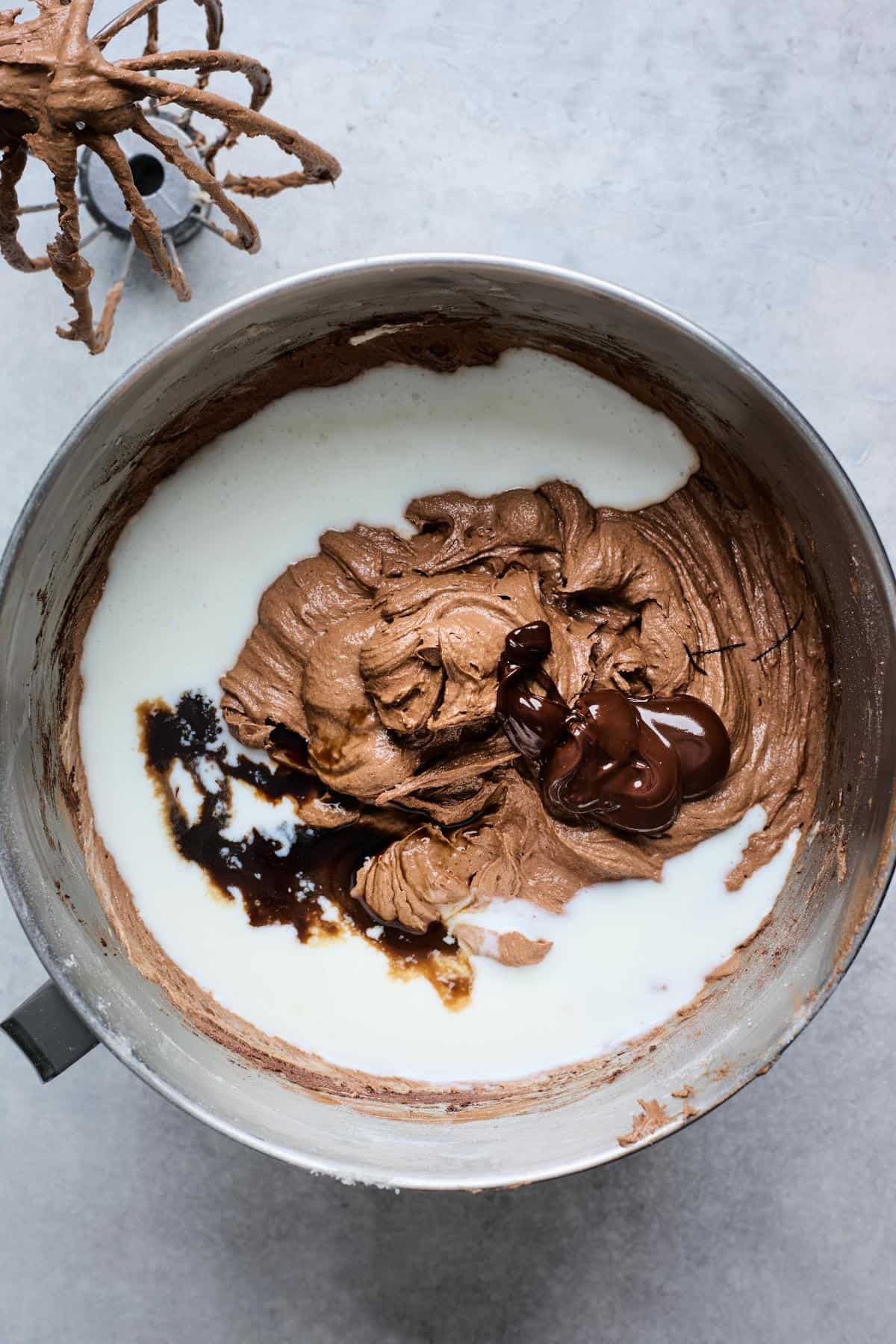 Chocolate batter in a mixing bowl, with melted chocolate, vanilla extract, and buttermilk added for blending