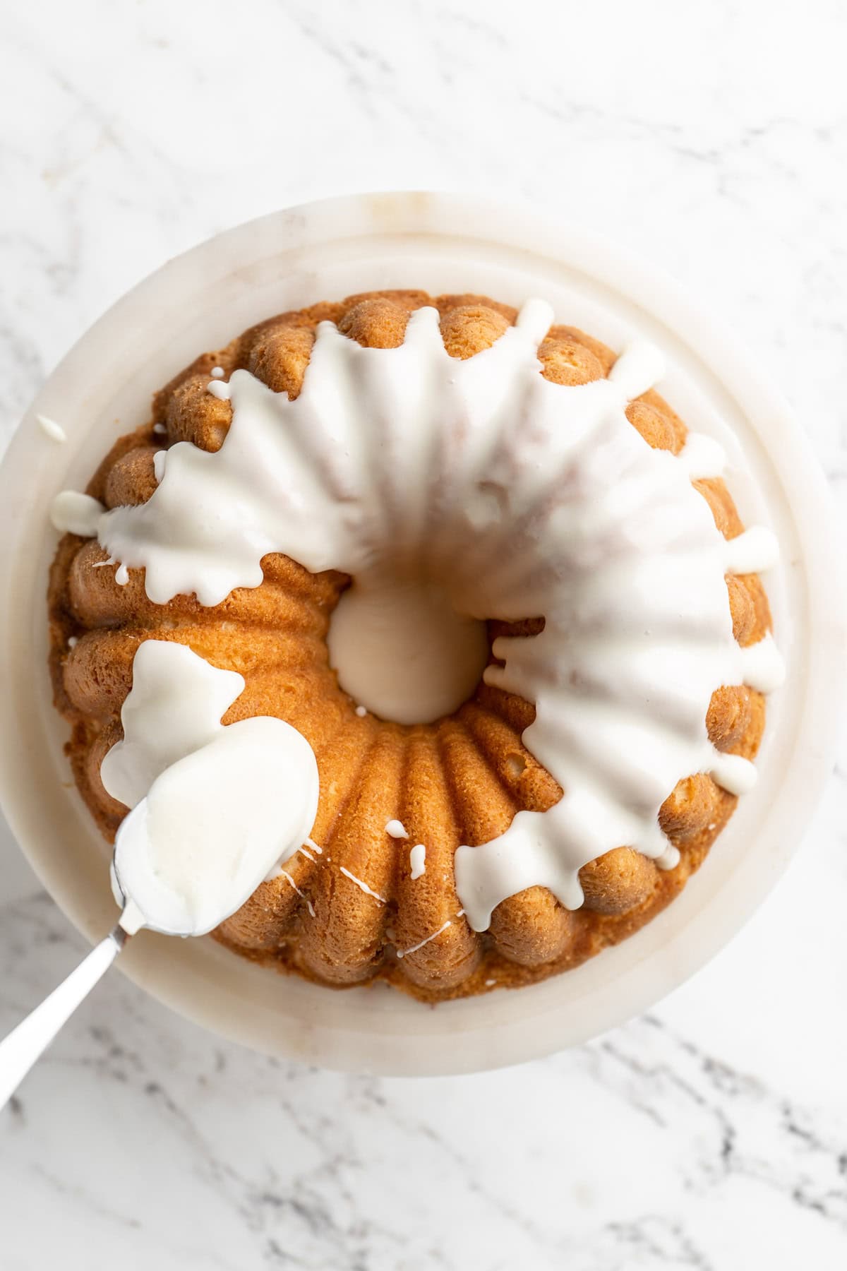 Glaze being added to coconut bundt cake recipe with a spoon