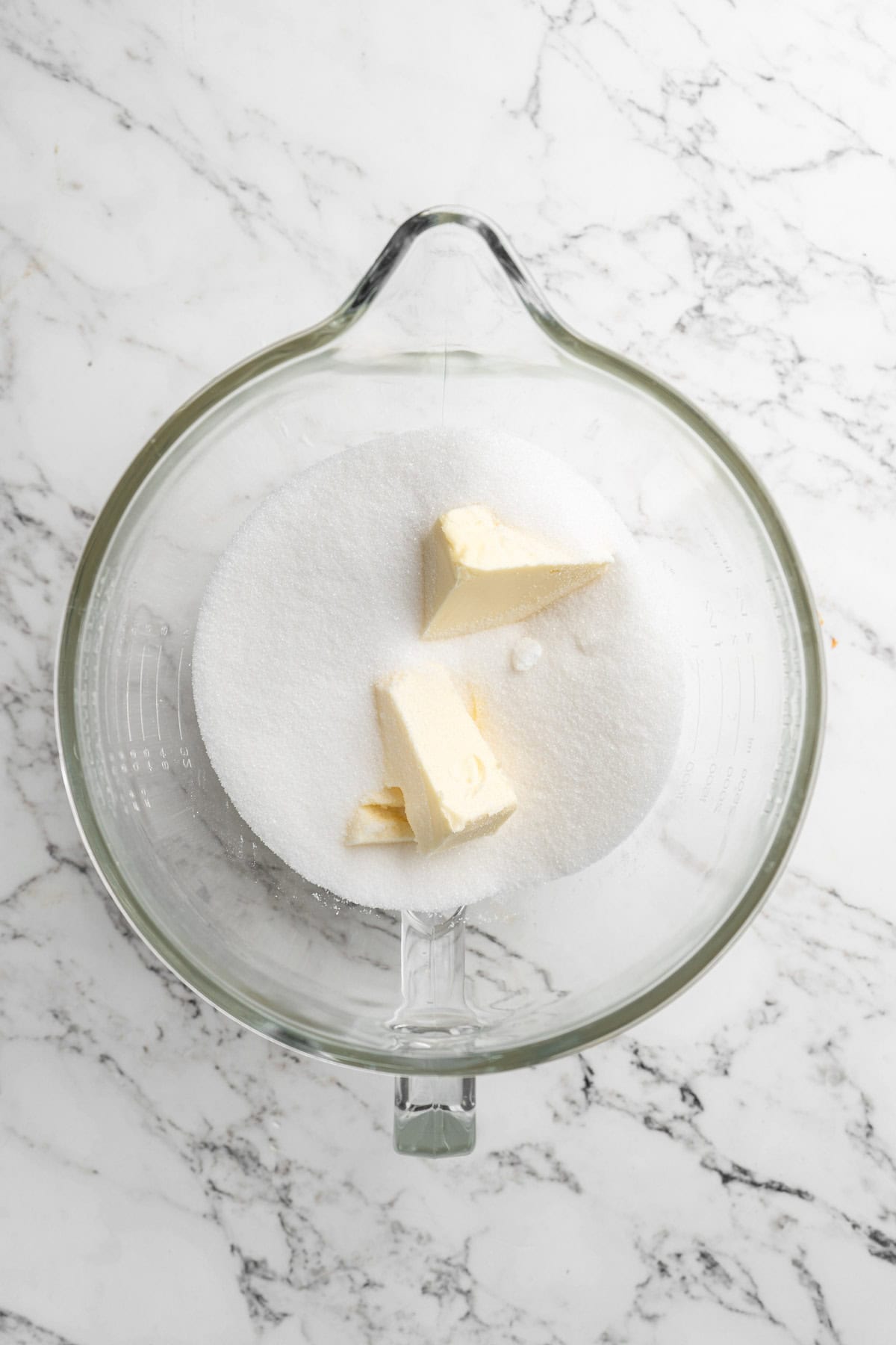 Butter and sugar in a glass stand mixer bowl on white marble countertop