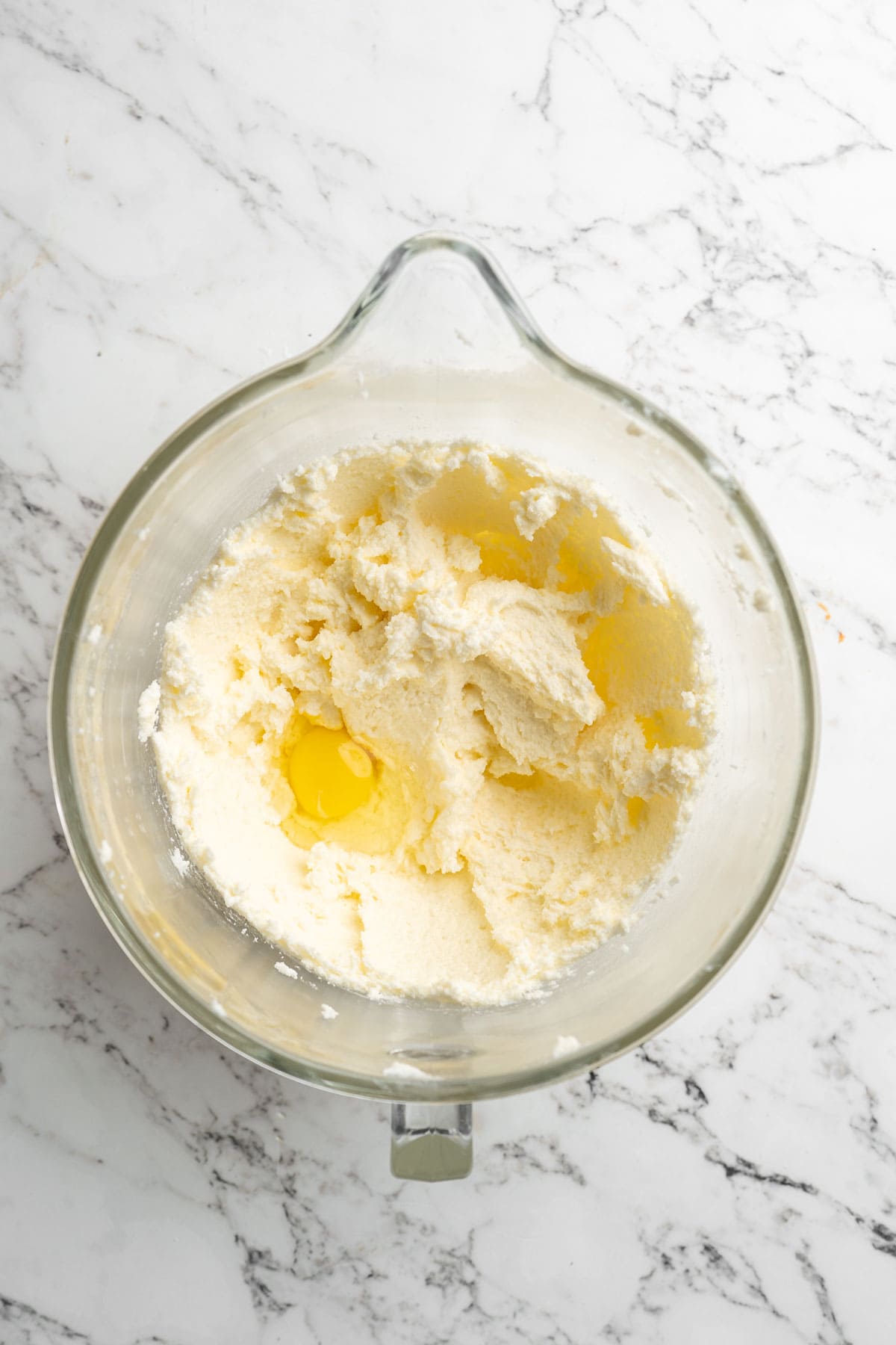 Eggs being added to a pound cake batter in glass stand mixer on white countertop