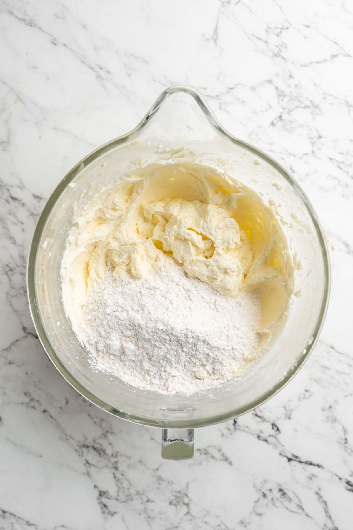 Flour being added to coconut pound cake batter in stand mixer bowl on white marble countertop.