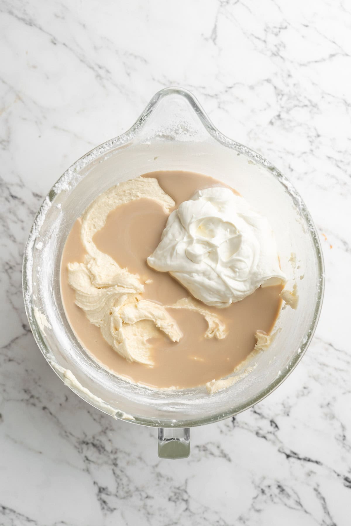 Sour cream, milk and extracts being added to stand mixer with cake batter on white countertop