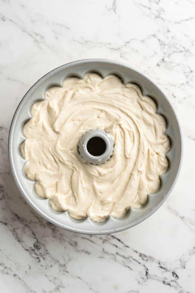 Cake batter poured into a greased bundt pan on white countertop.