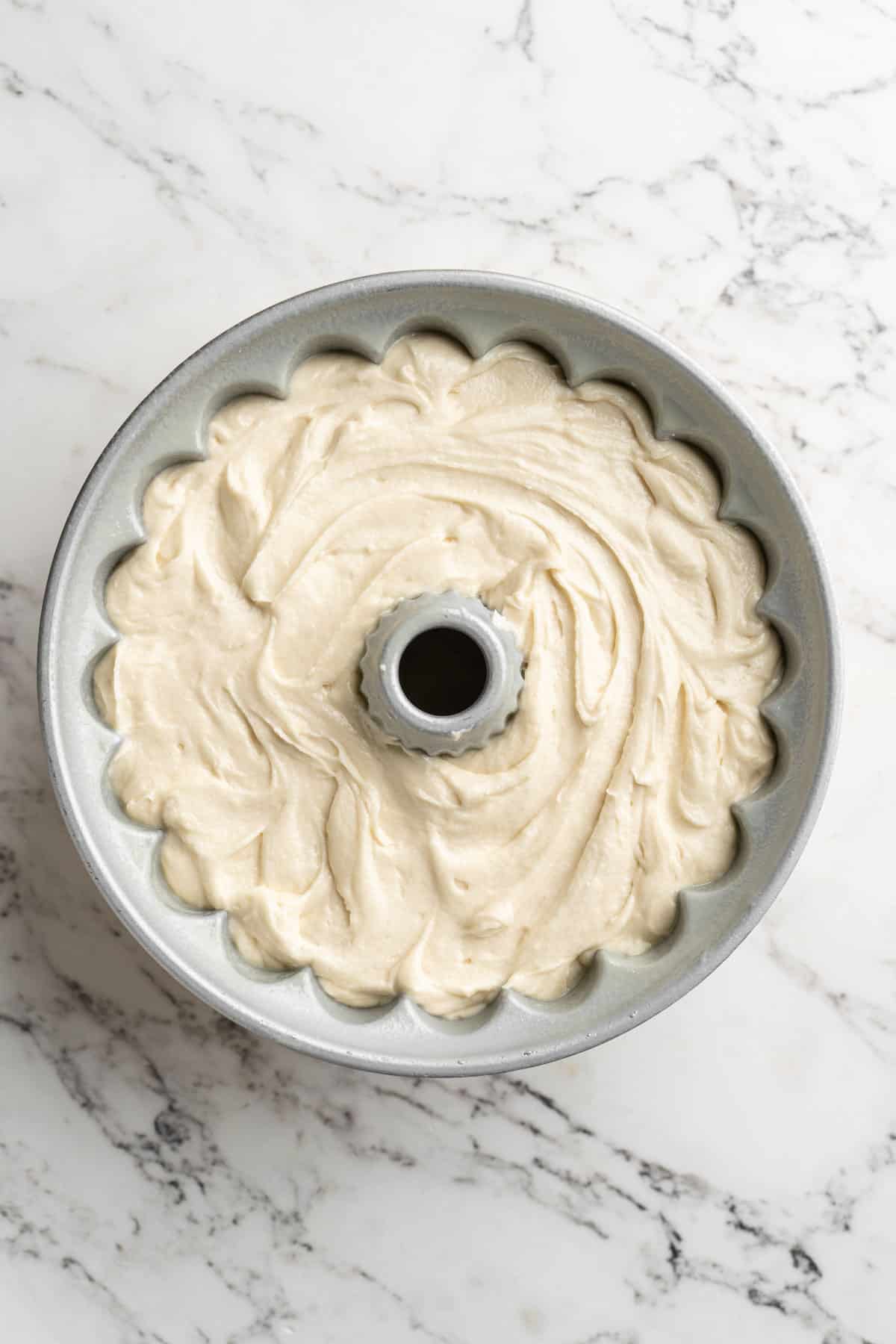 Cake batter poured into a greased bundt pan on white countertop.