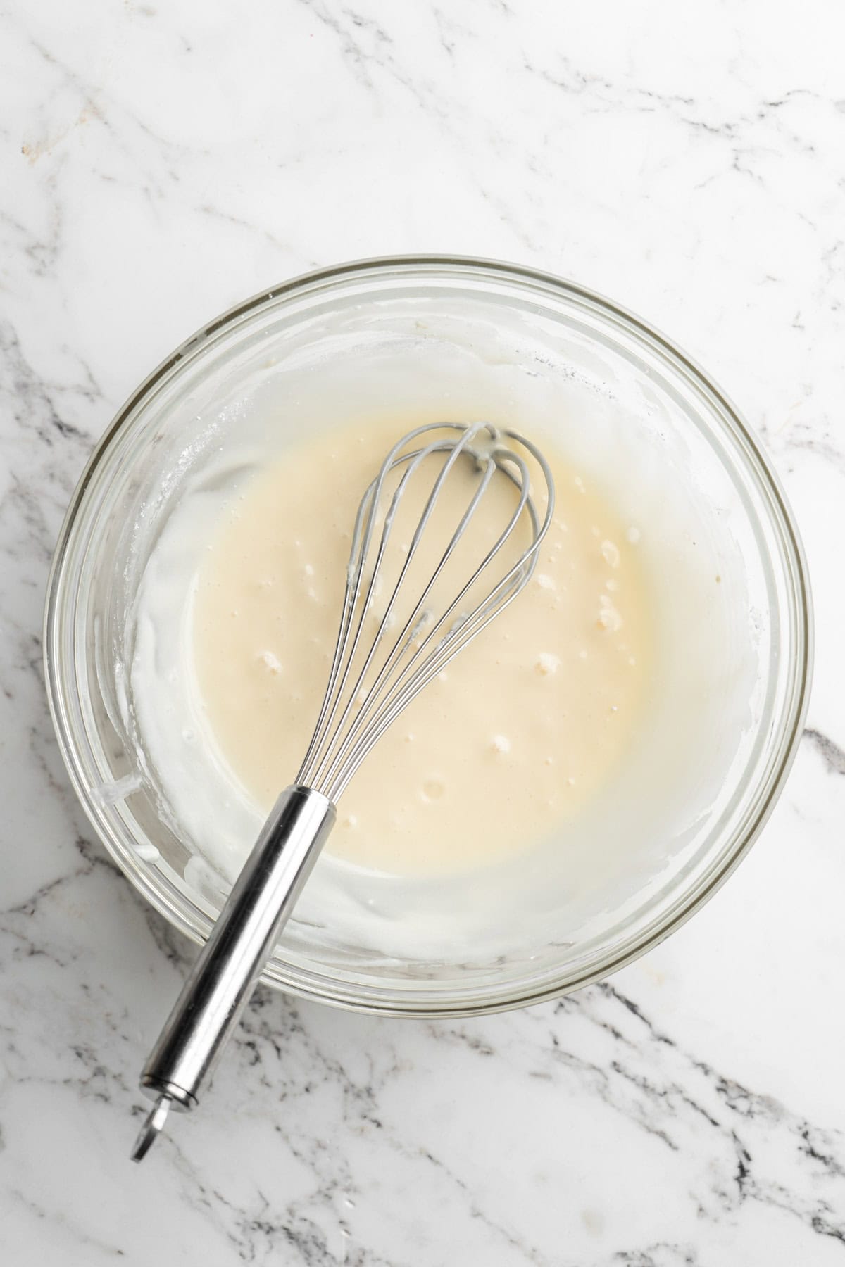 Coconut glaze in a glass bowl with a whisk on white countertop