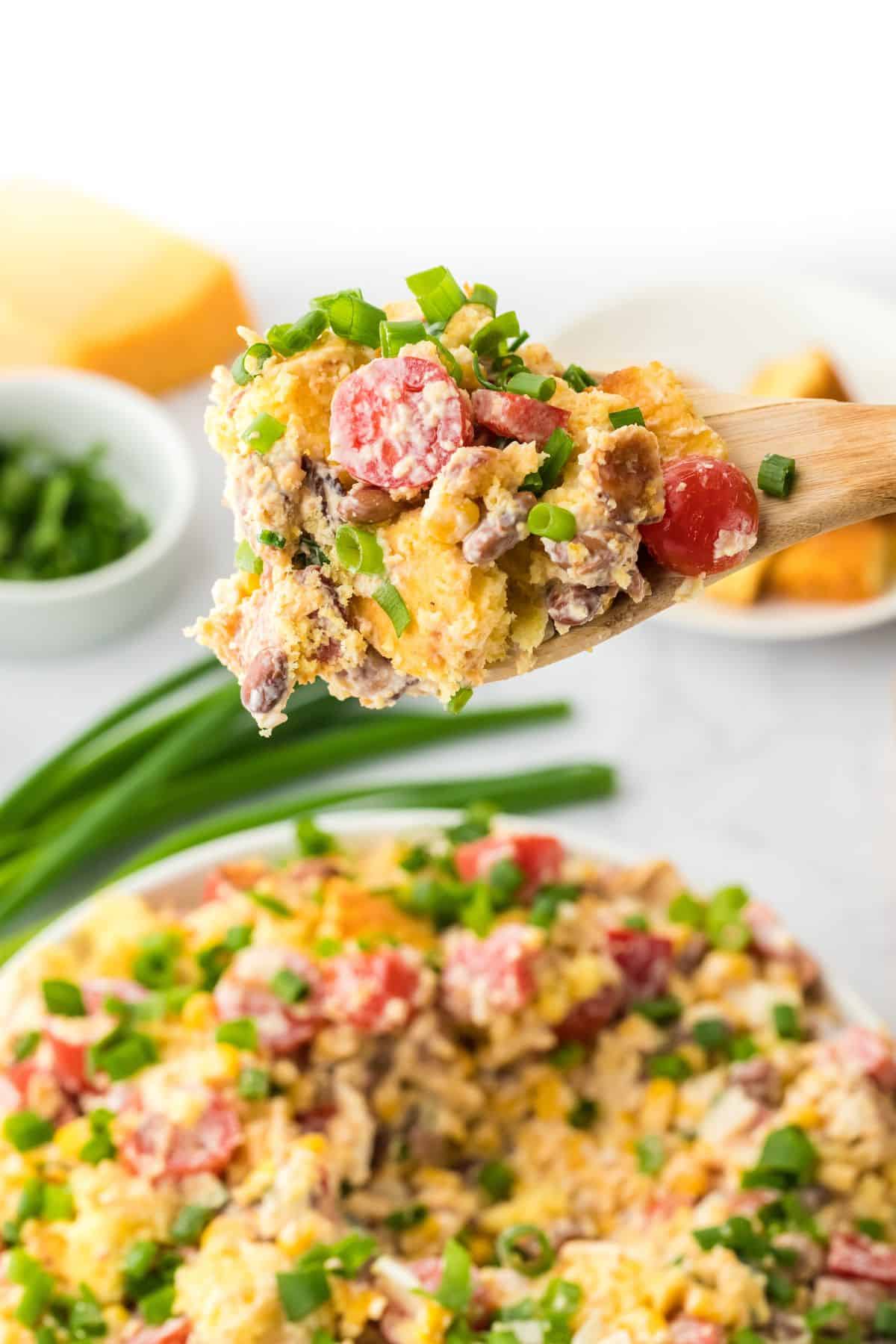 A spoon of cornbread salad lifting from a large bowl