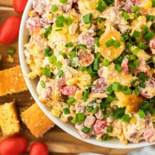 Overhead shot of cornbread salad garnished with green onions in a large white bowl with cornbread pieces and tomatoes in the background