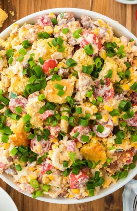 Overhead shot of cornbread salad garnished with green onions in a large white bowl