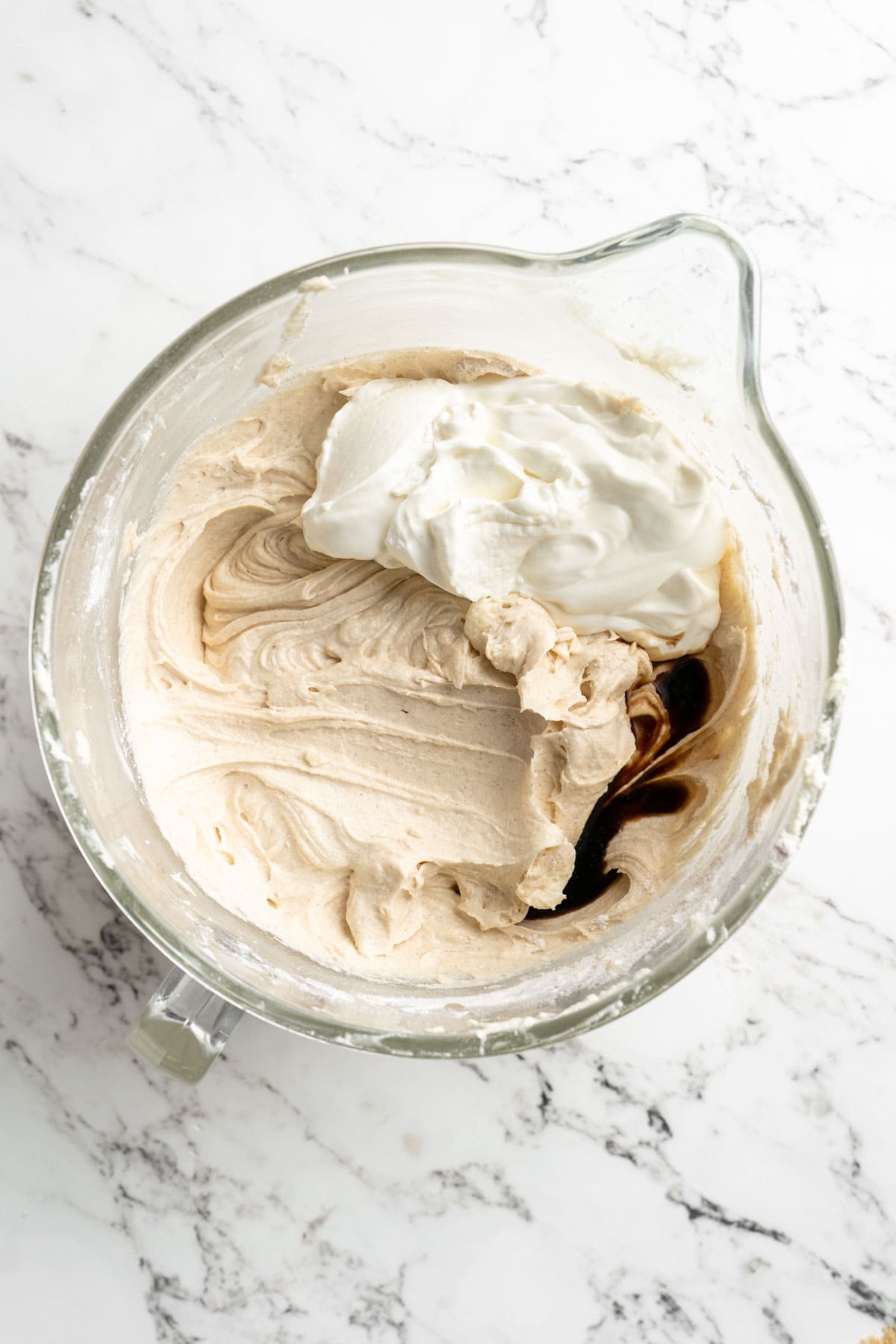 Sour cream and vanilla being added to a stand mixer with cake batter on white countertop