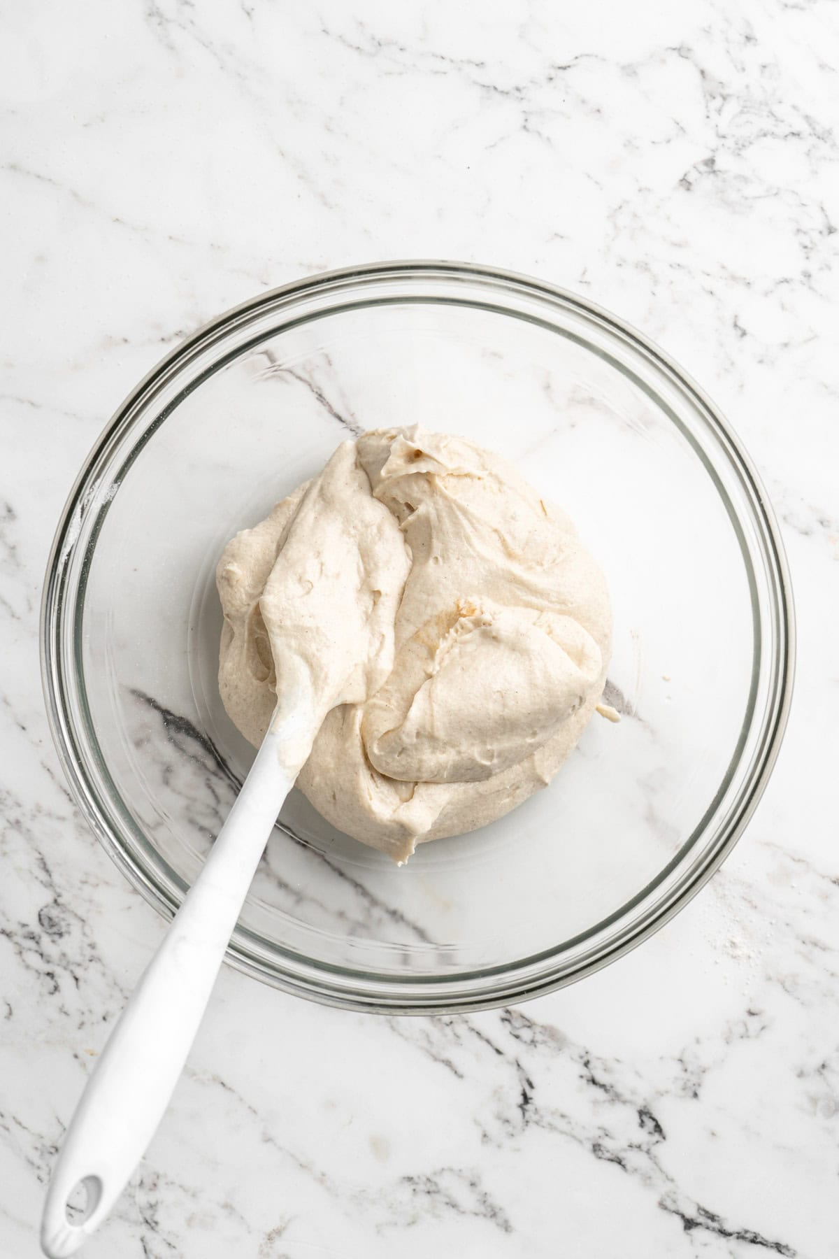 Cake batter separated into a glass bowl with a spatula on white countertop