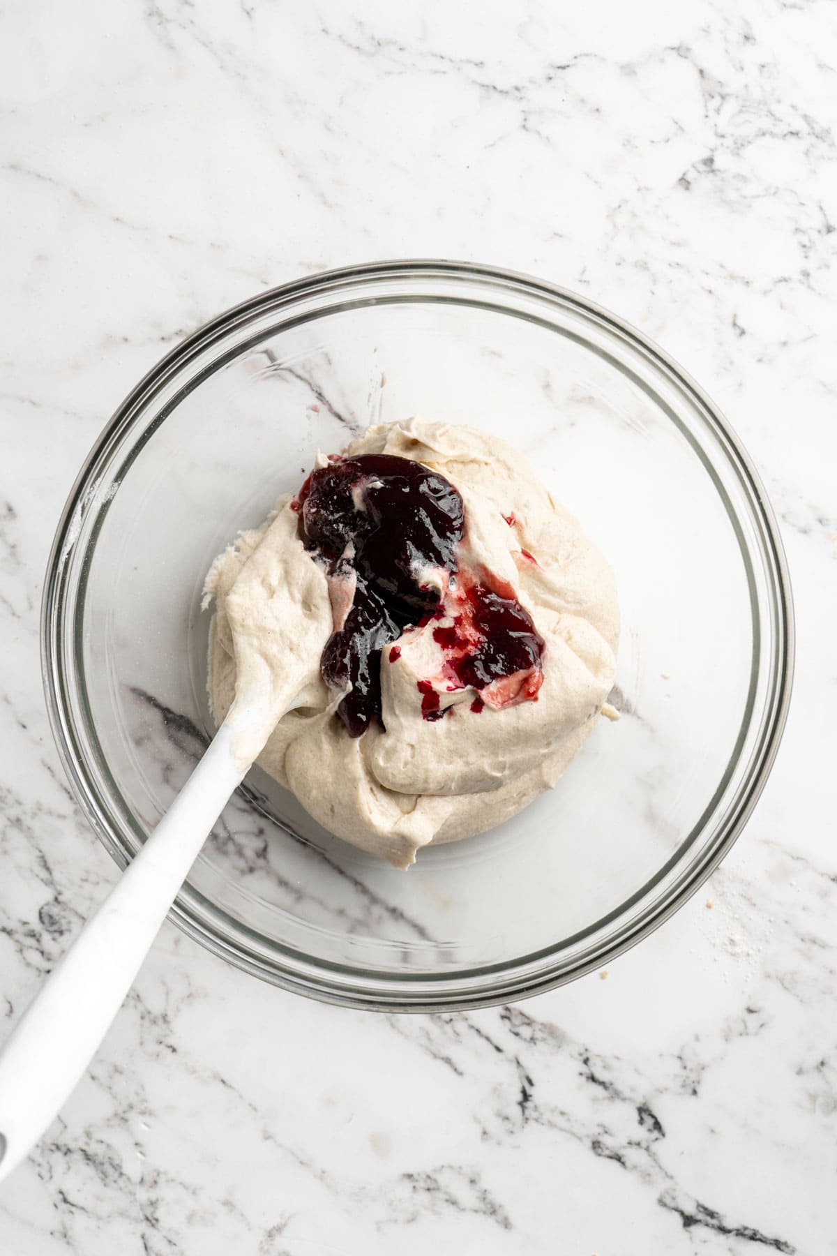 Melted raspberry jam and food coloring added to a cake batter in a glass bowl