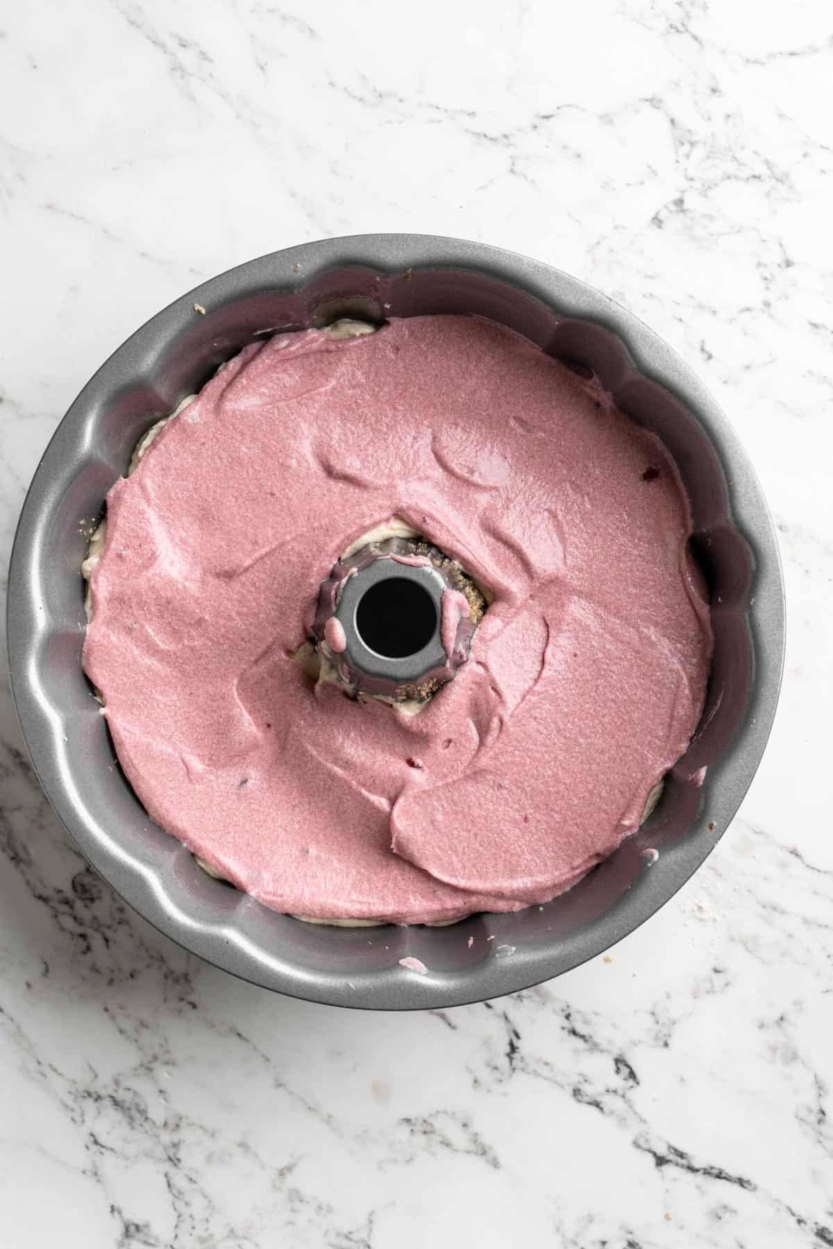 Cranberry batter added on top of bundt pan on white countertop