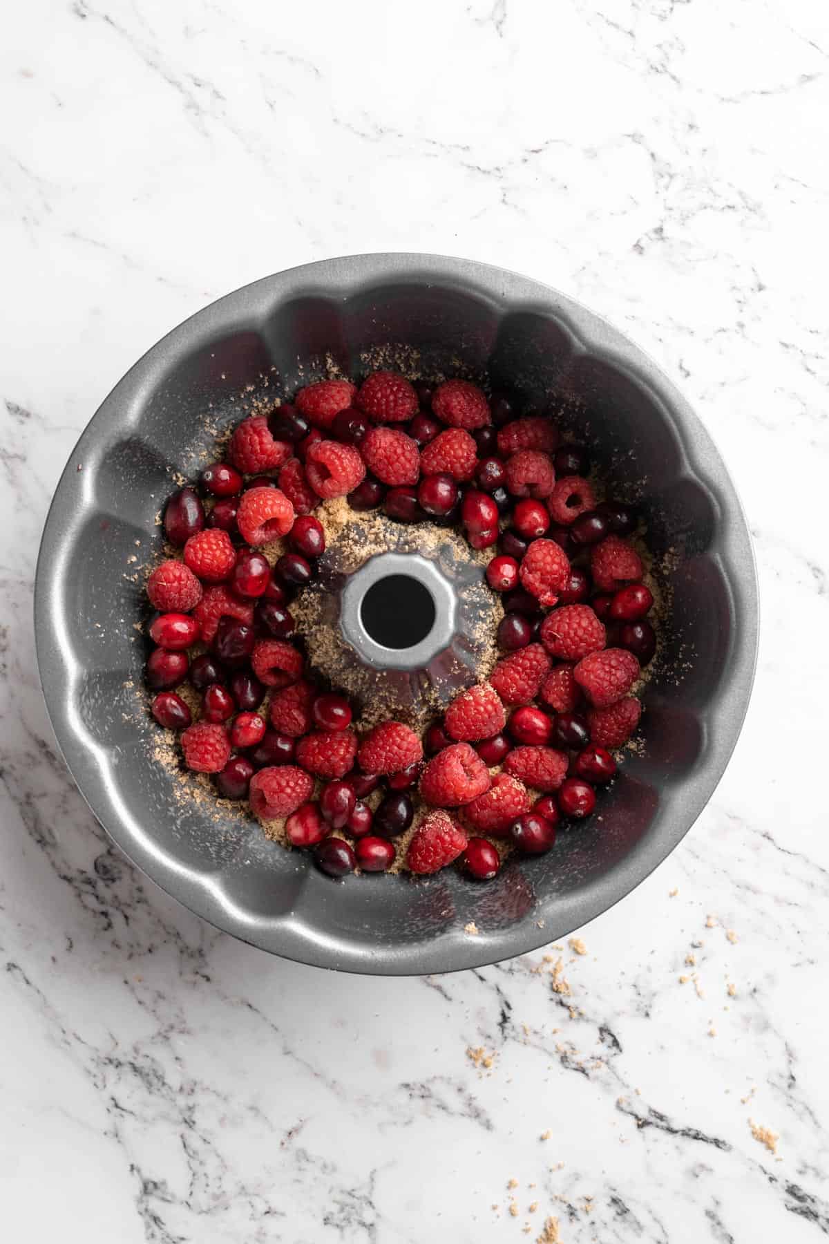 A mix of cranberries and raspberries on the bottom of a bundt pan on white countertop