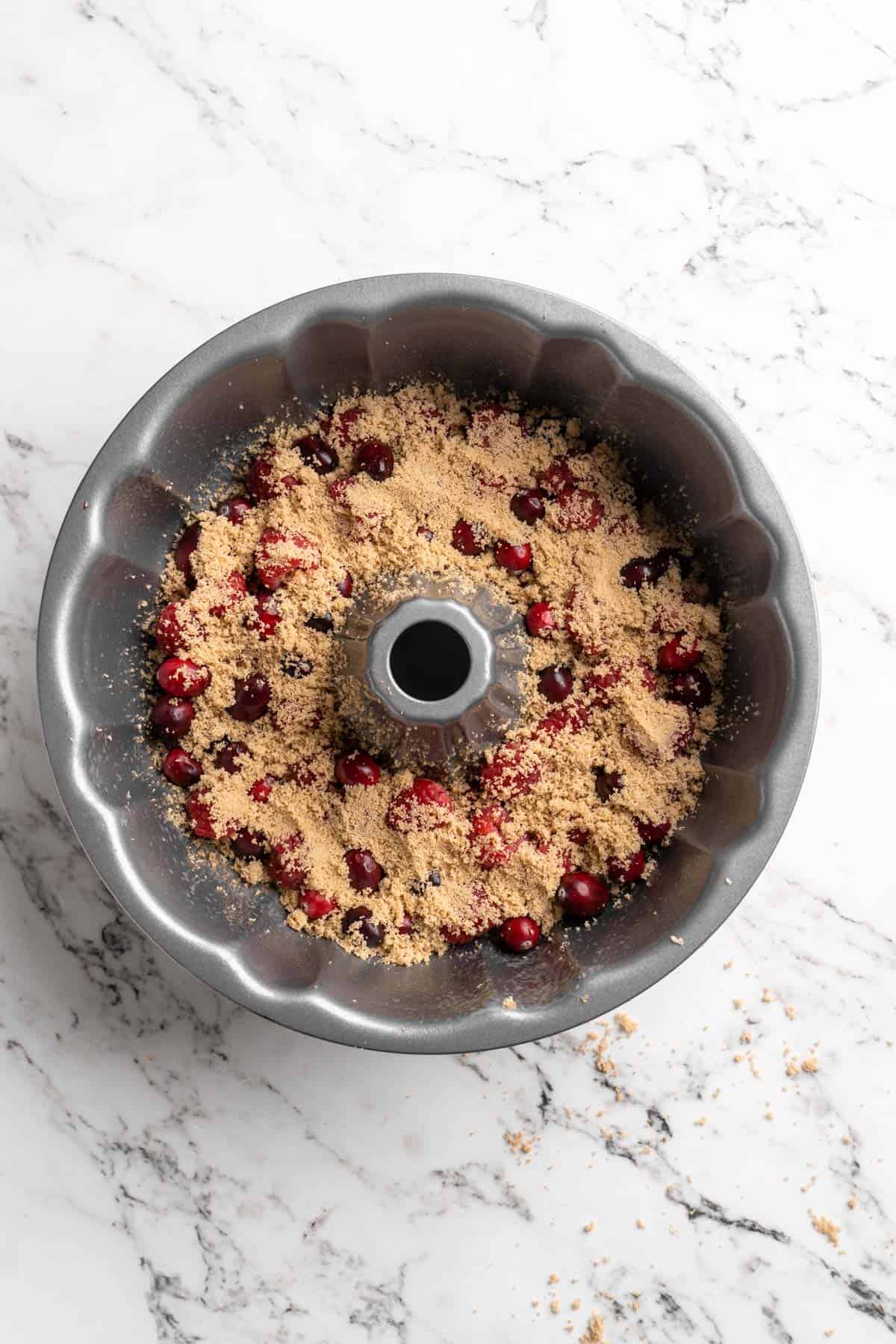 Brown sugar sprinkled on top of berries in bottom of a bundt pan on white countertop